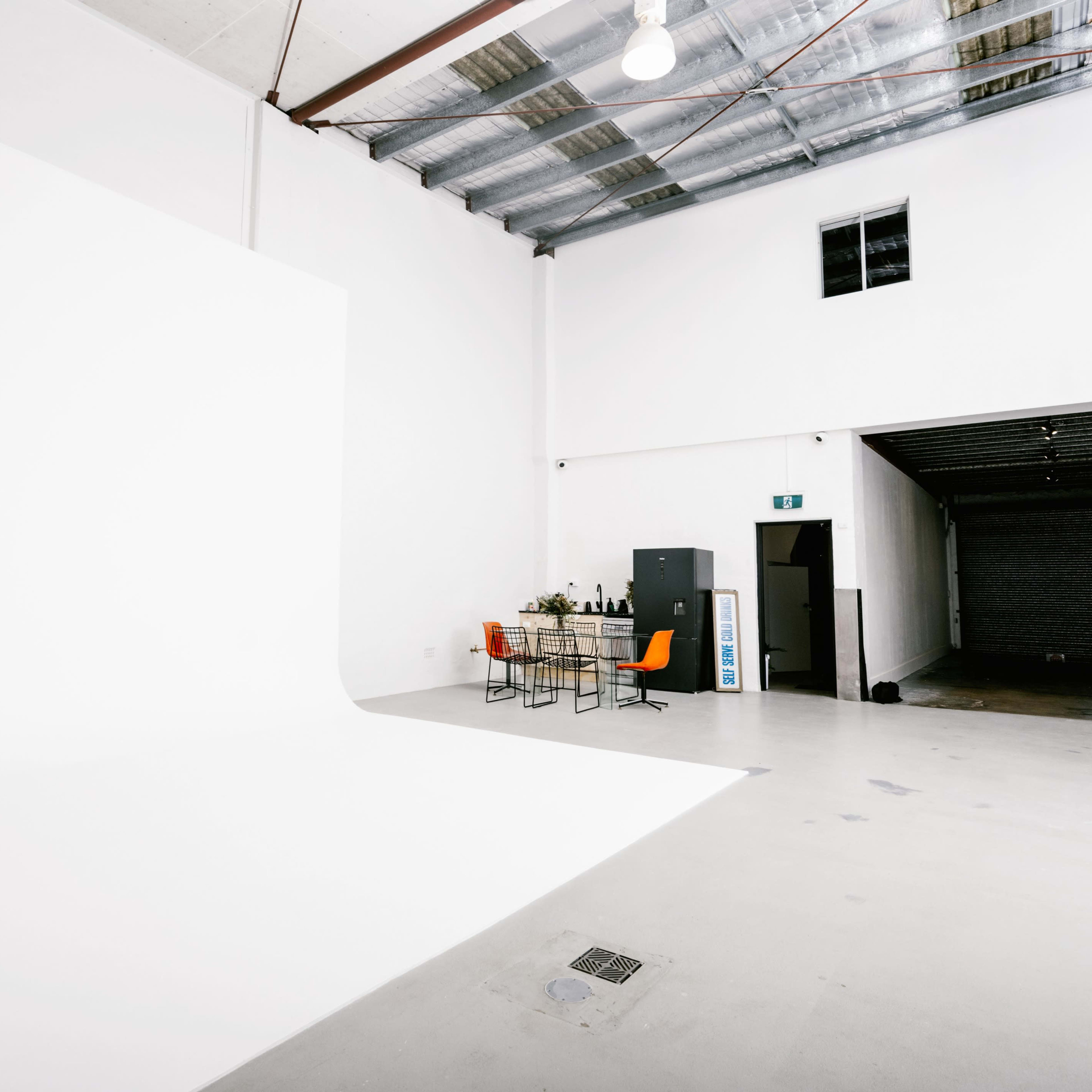 A spacious, empty studio with a white backdrop, a table set with chairs, and a gray cabinet against one wall.