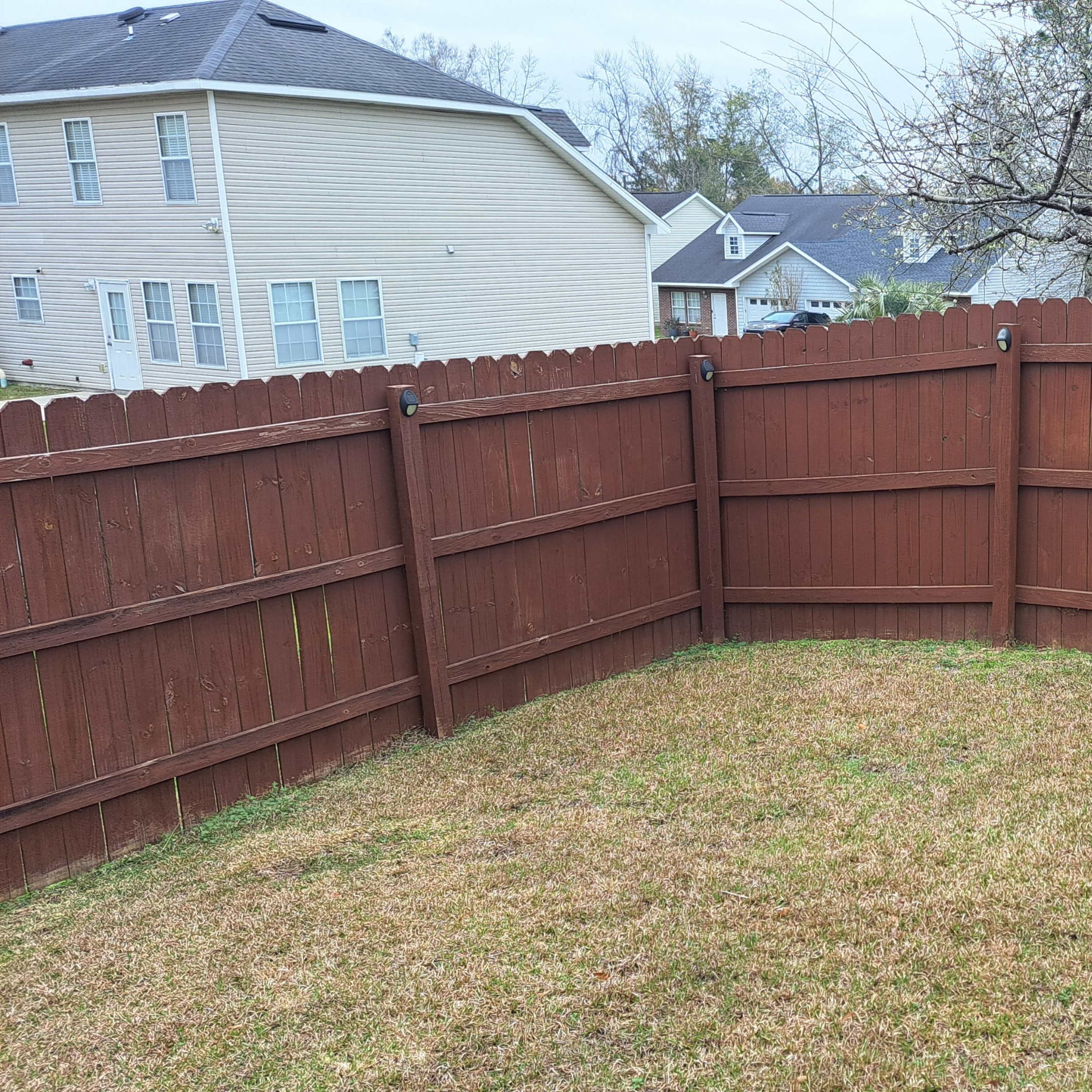 A section of a fenced backyard with a brown wooden fence enclosing a grassy area.