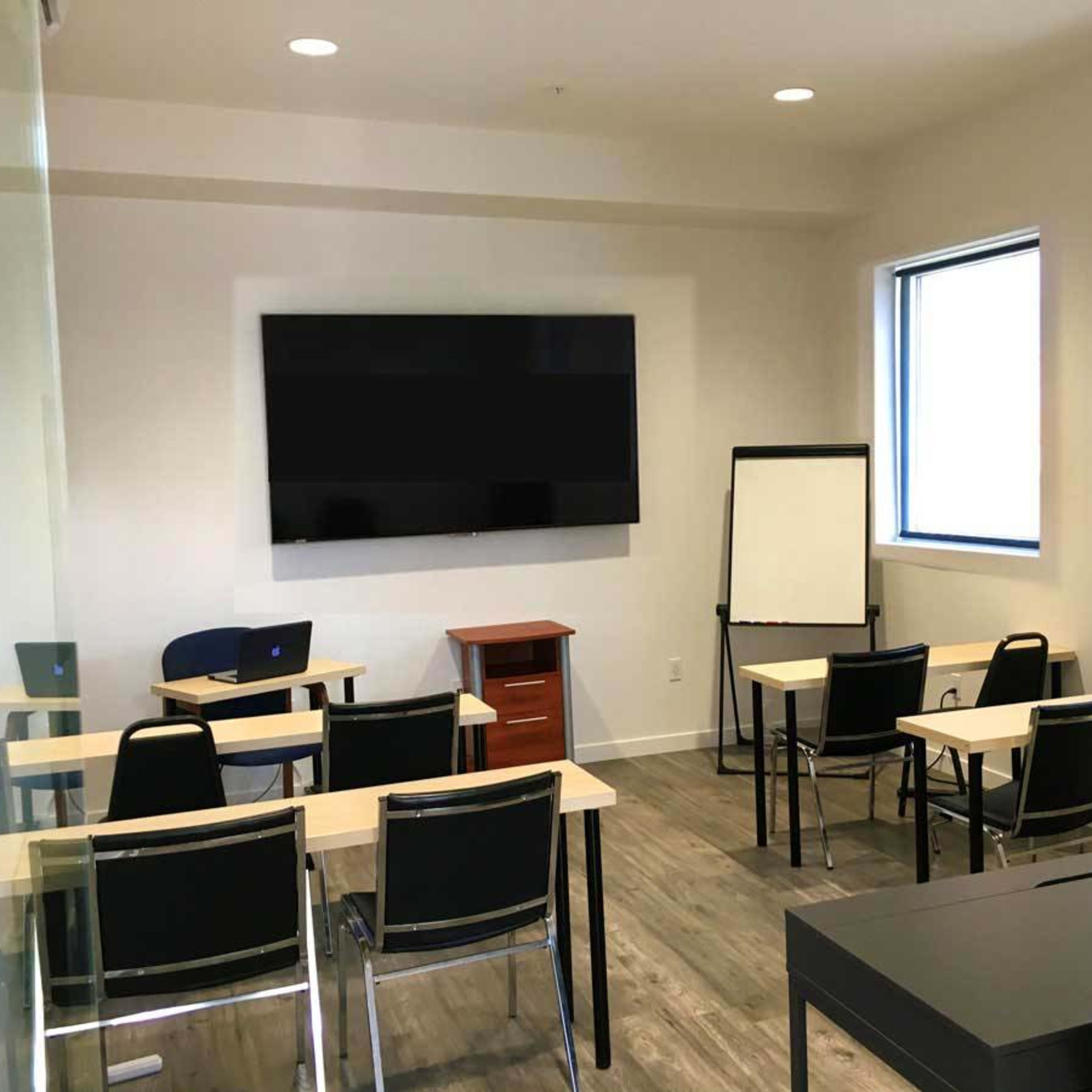A modern classroom equipped with a large wall-mounted screen, several tables, chairs, and a writing board.