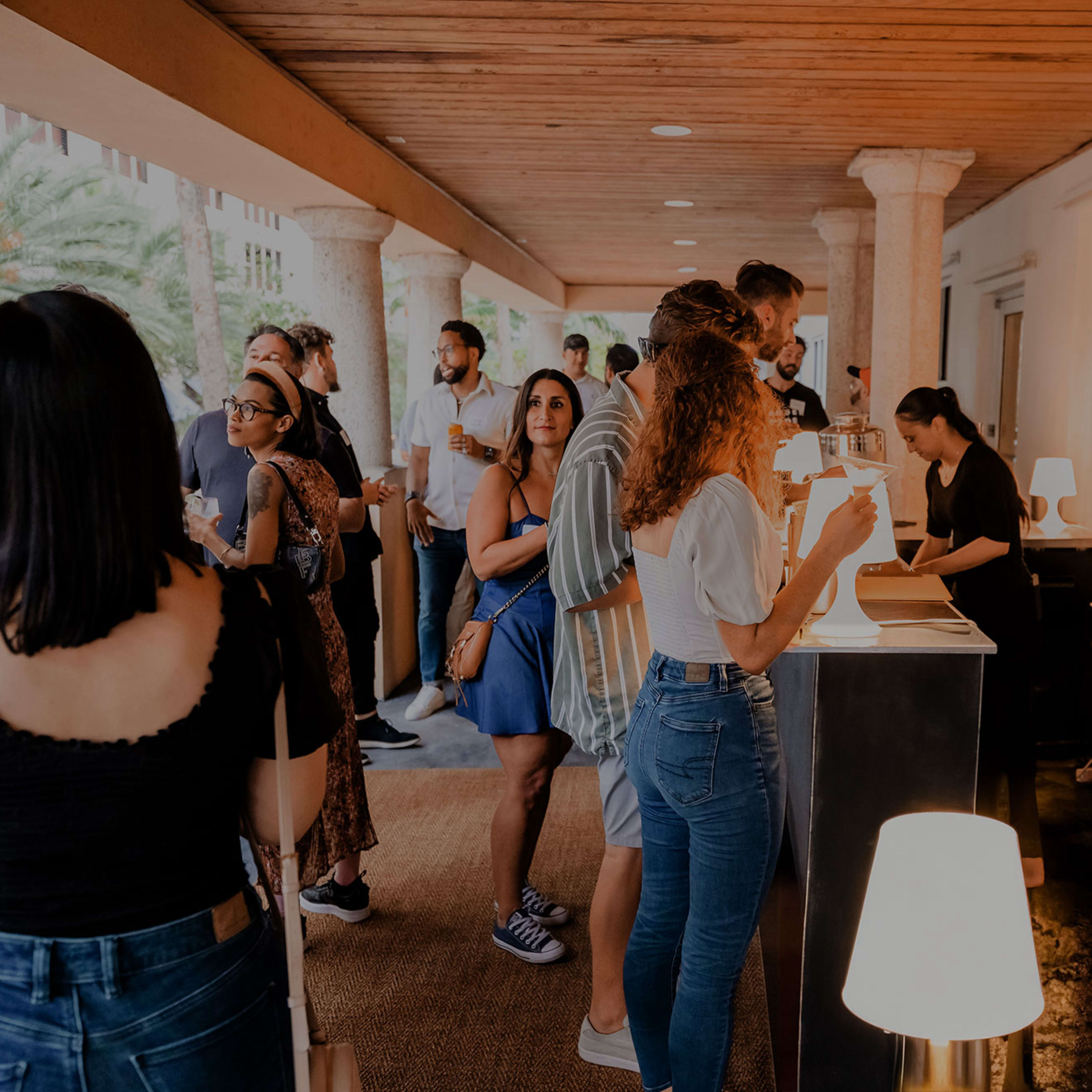 A group of people is gathered at a reception area with a service counter, chatting and interacting under a covered outdoor space.