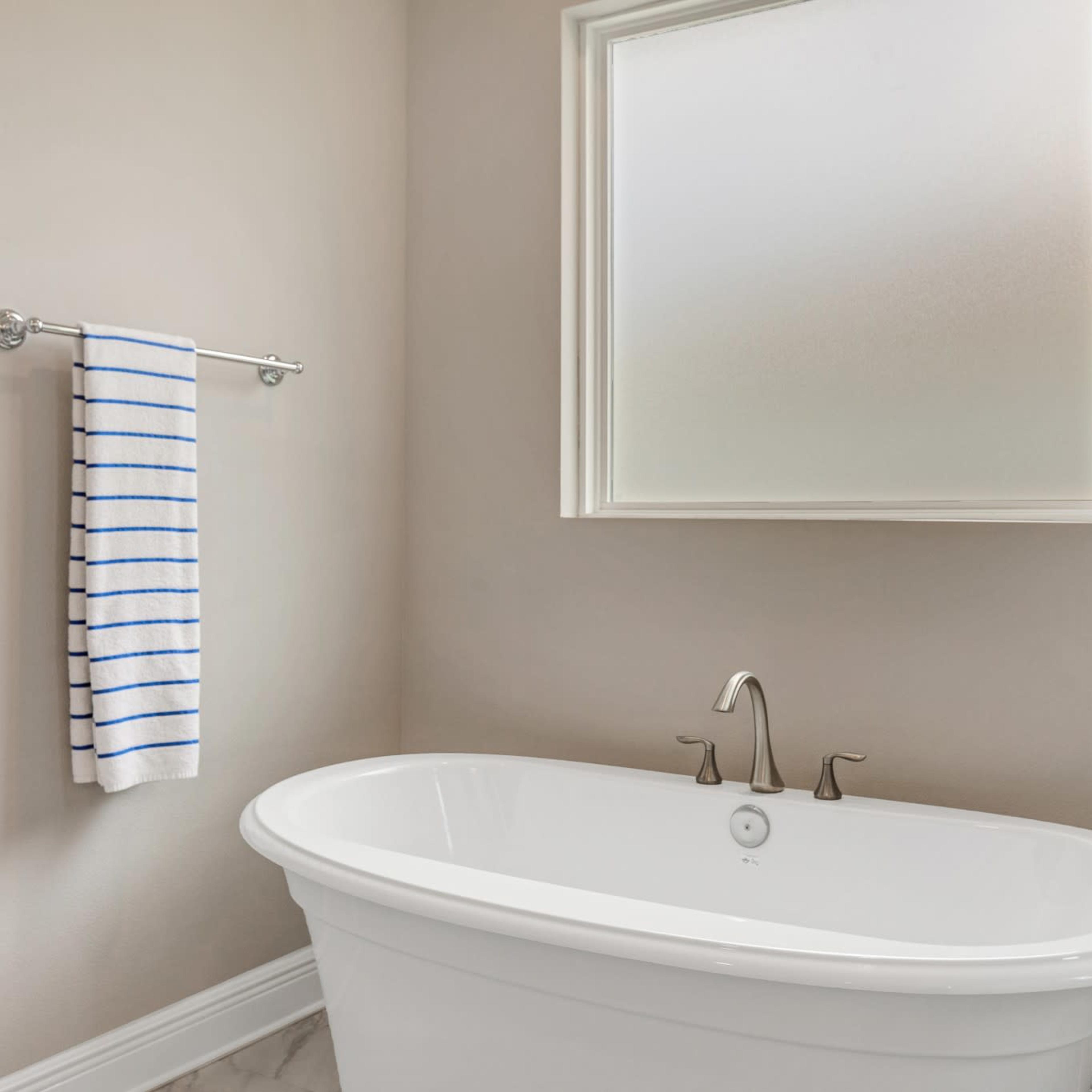 A bright bathroom featuring a freestanding white bathtub, a glass shower enclosure, and a white towel with blue stripes hanging on a towel rack.