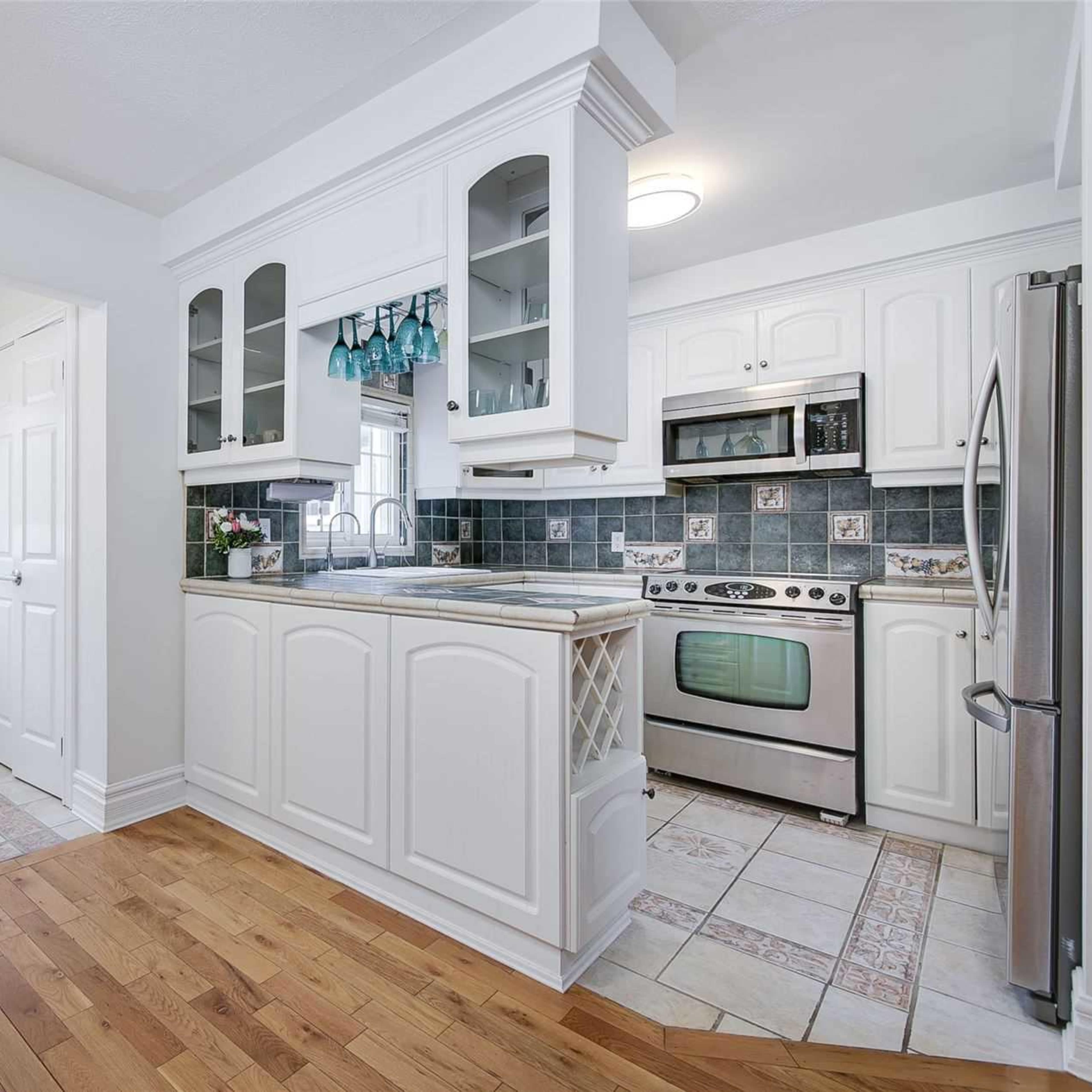 A well-lit kitchen featuring white cabinetry, stainless steel appliances, and tiled flooring, with a door leading outside.
