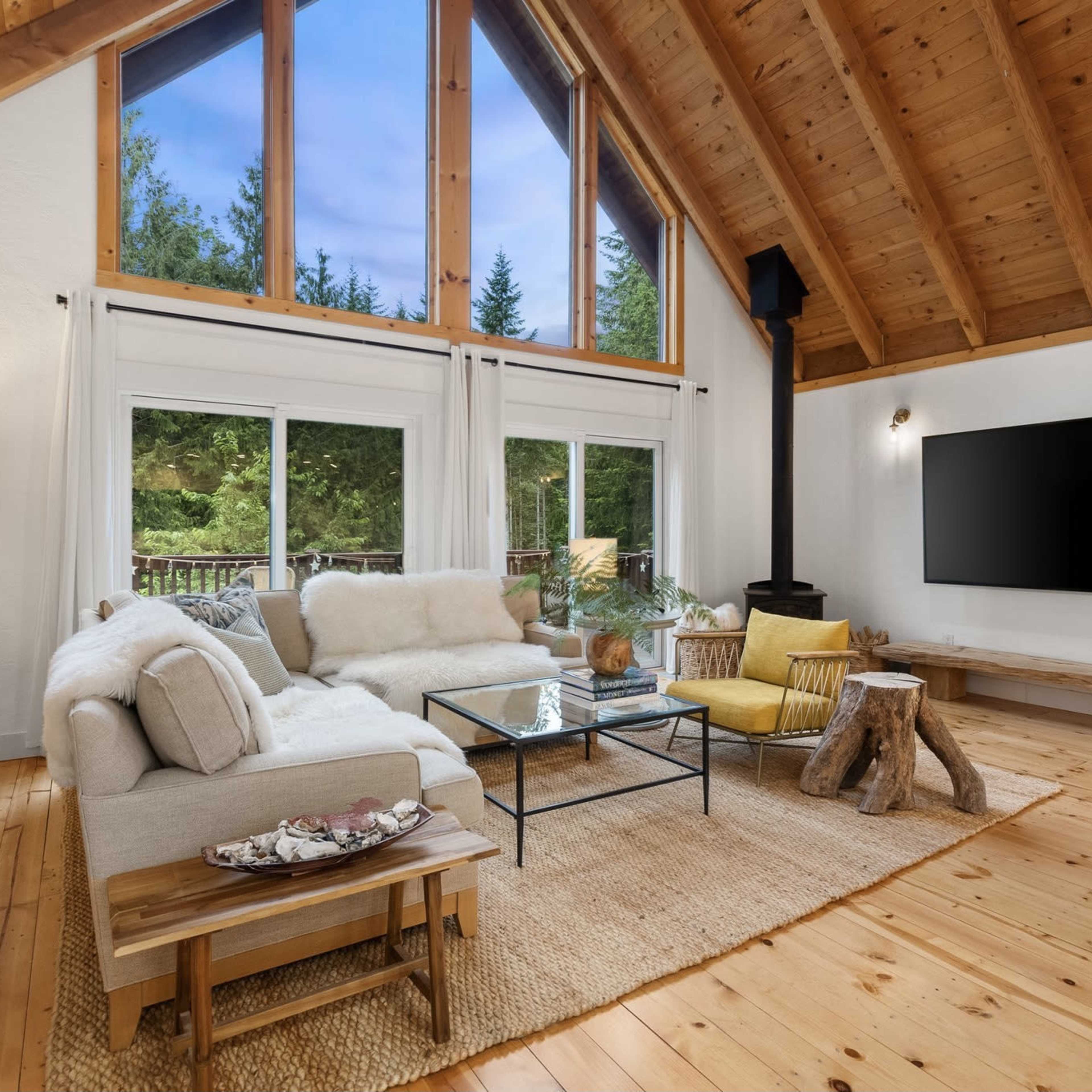 A spacious living room features a large sectional sofa, a glass coffee table, and a flat-screen TV mounted on a wooden wall.
