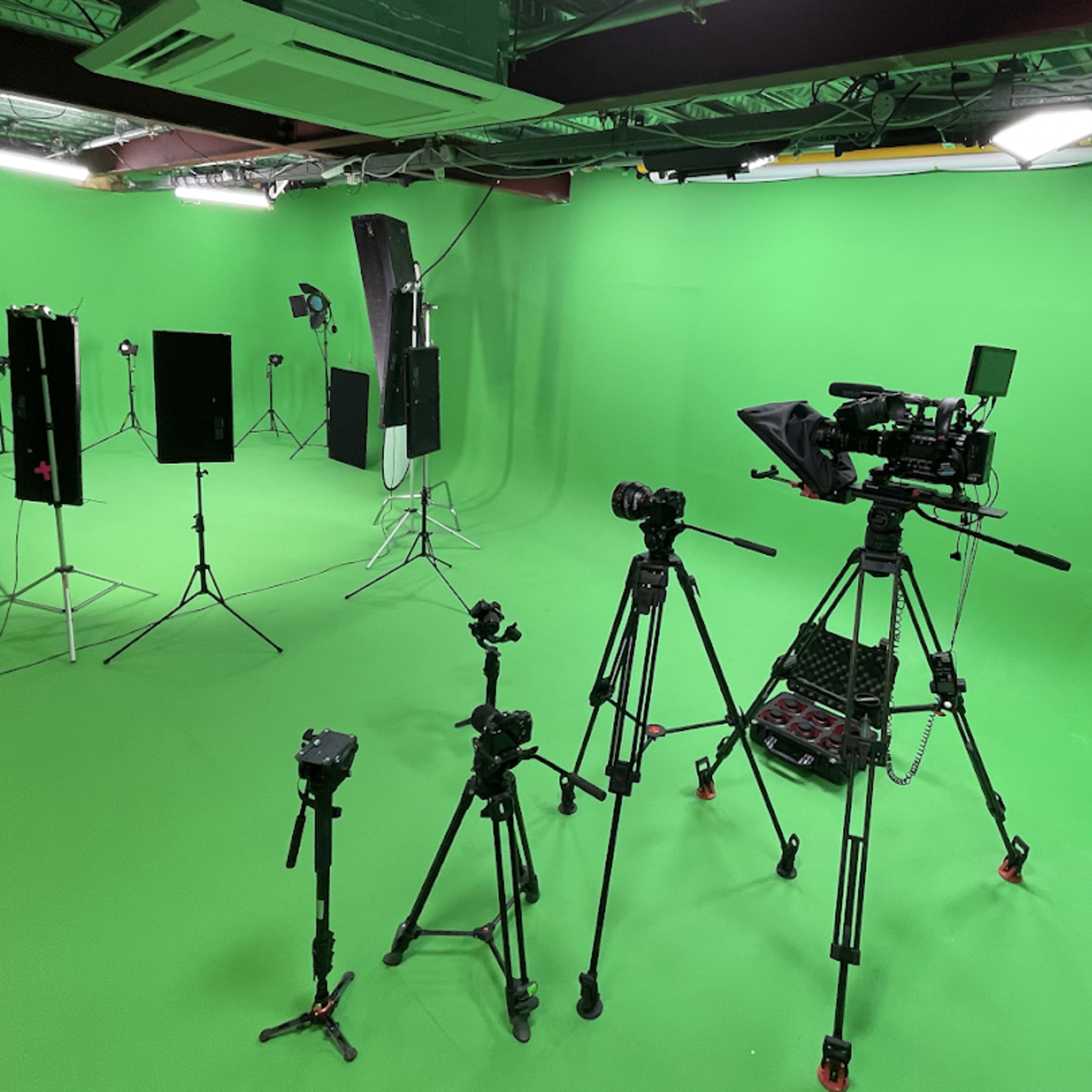 A green-screen studio equipped with various cameras and lighting equipment set up on tripods.