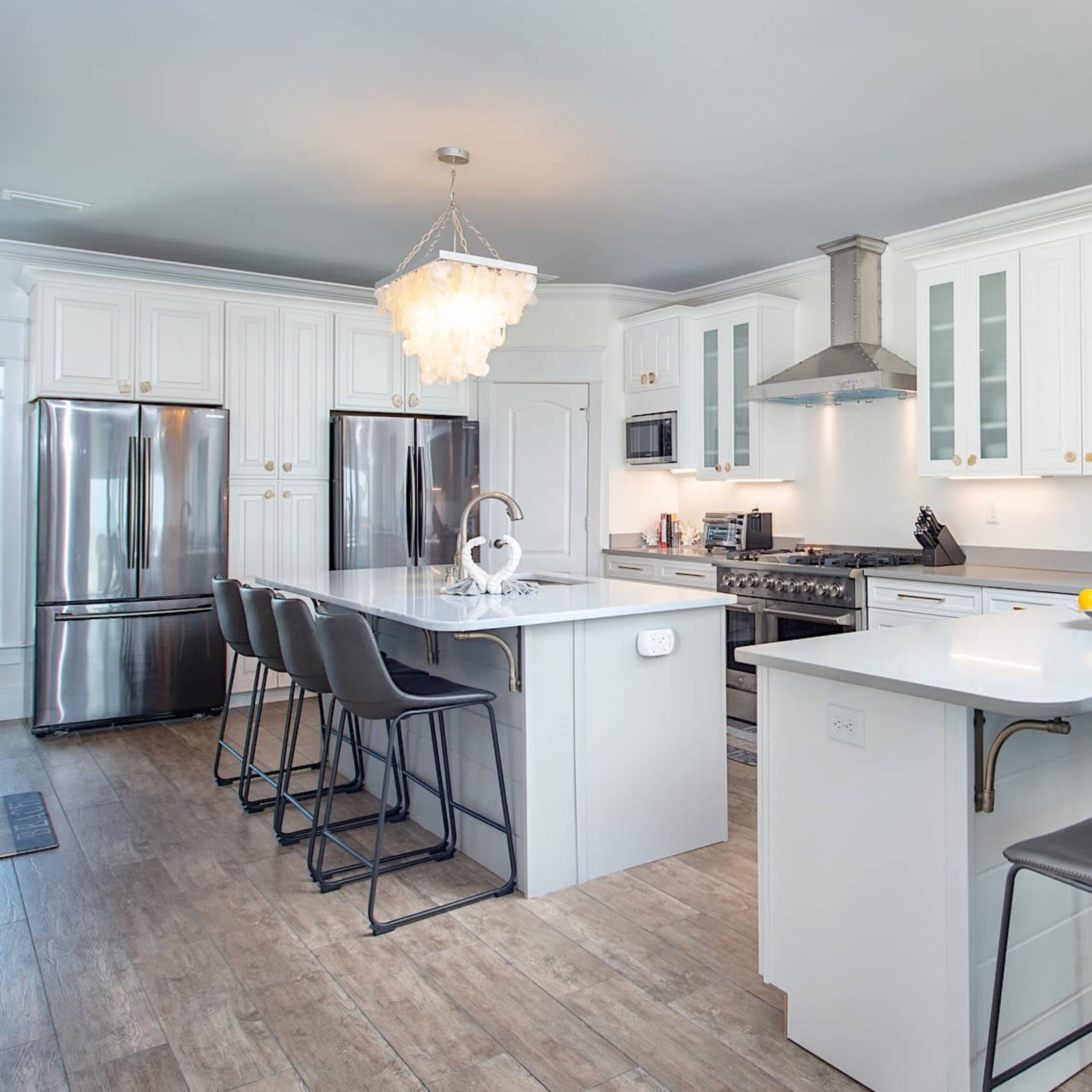 A modern kitchen featuring white cabinets, stainless steel appliances, a large central island with seating, and a decorative chandelier.