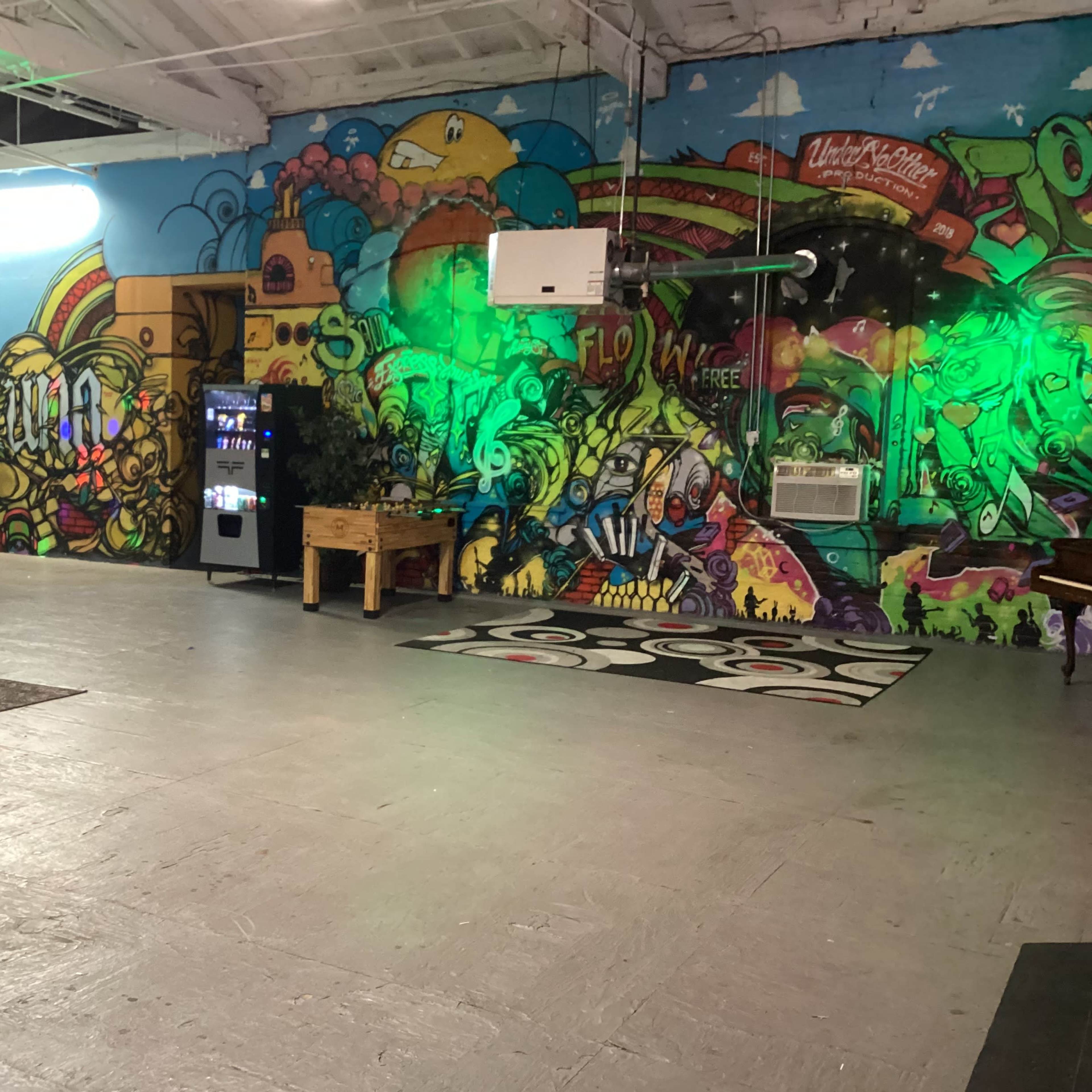 A spacious room with colorful graffiti murals on the walls, a pool table area, and a vending machine in the corner.