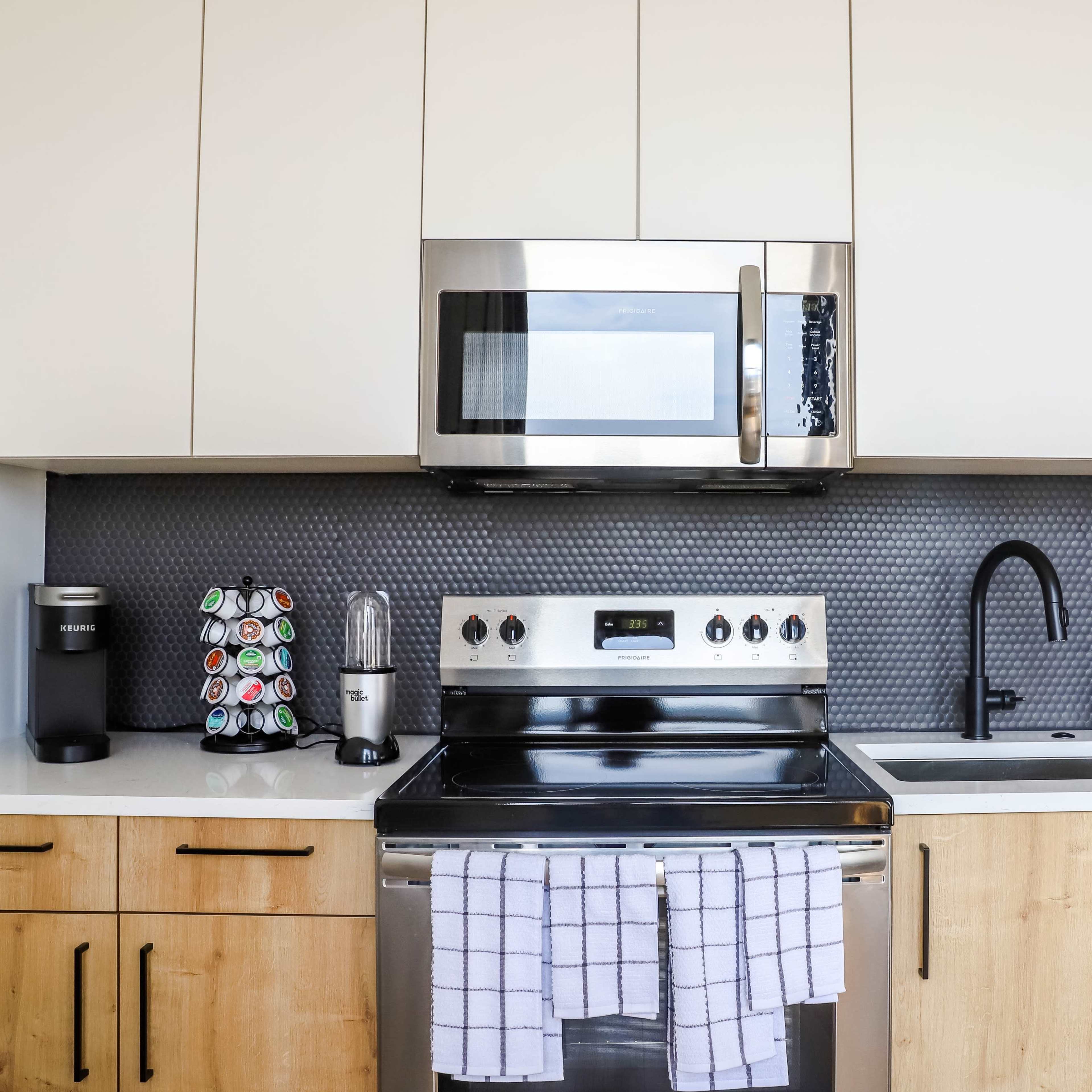 A modern kitchen features stainless steel appliances, wooden cabinets, and a black tile backsplash.