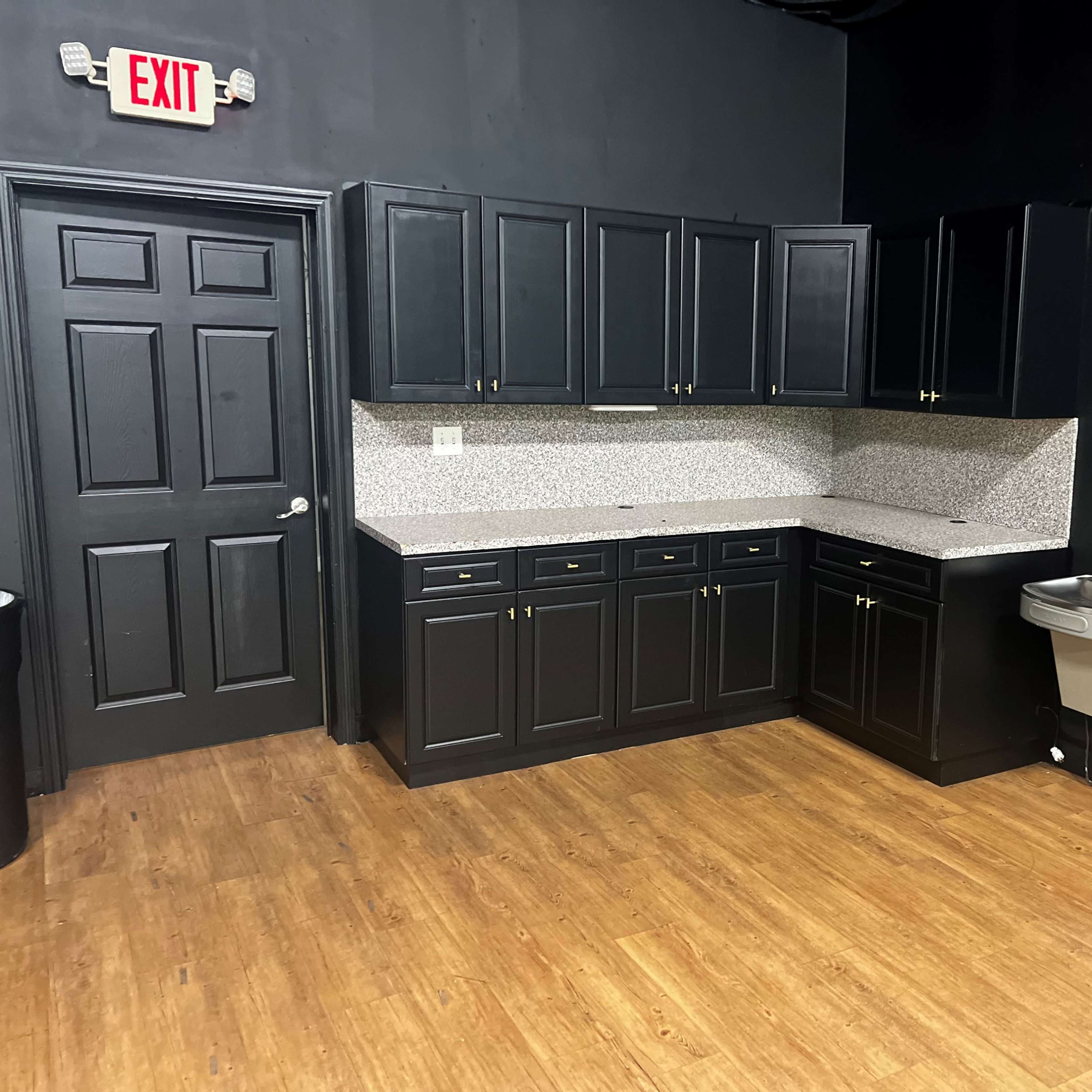 A kitchen with black cabinetry, a speckled countertop, and a metal sink against a dark wall.