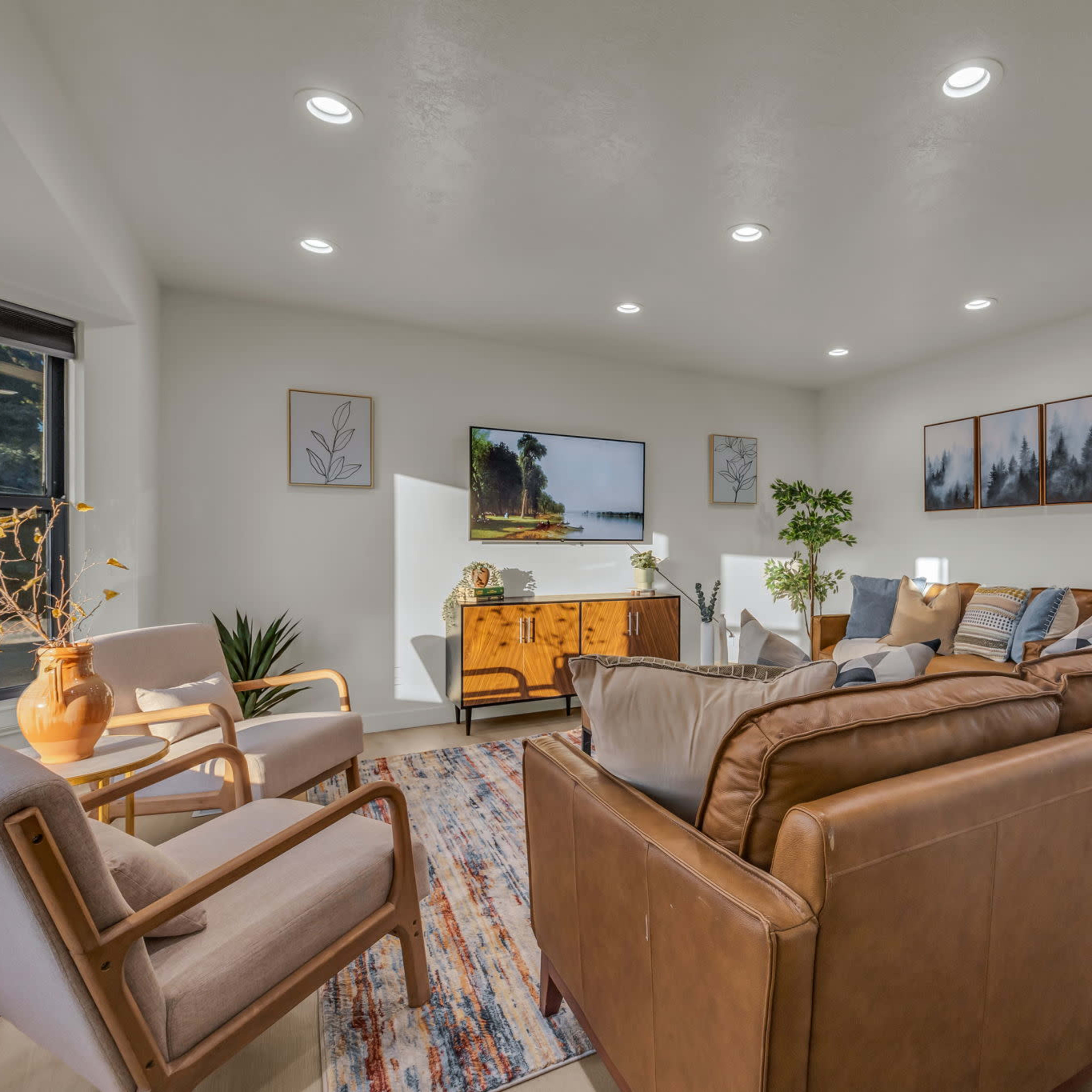 The living room features a leather sofa, two armchairs, and a wooden sideboard, illuminated by recessed lighting and decorated with framed art.