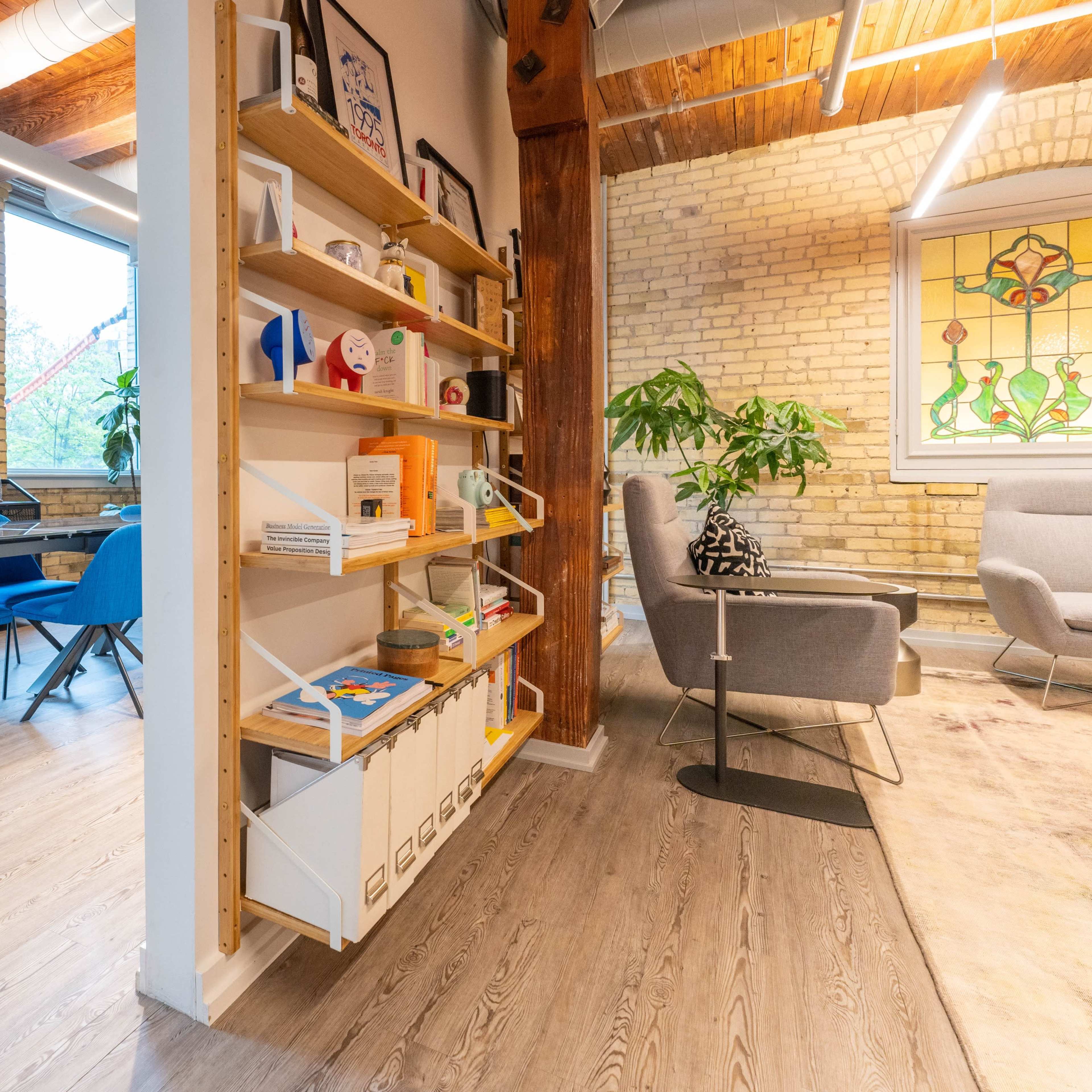 A modern interior space featuring a wooden shelving unit filled with various items, a seating area with gray furniture, and a dining area with blue chairs.