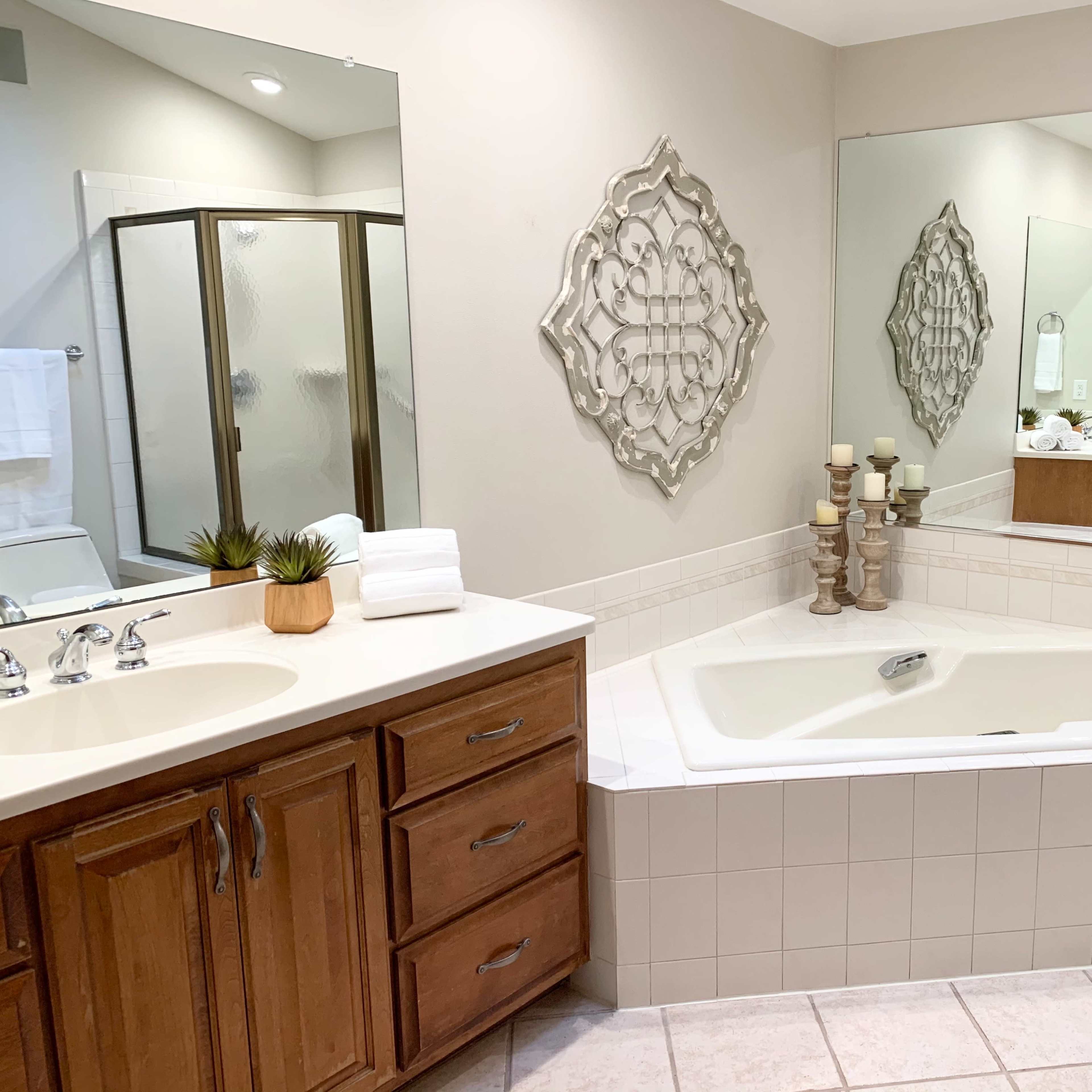 A well-lit bathroom featuring a large bathtub, double sinks with wooden cabinets, and a separate glass shower stall.