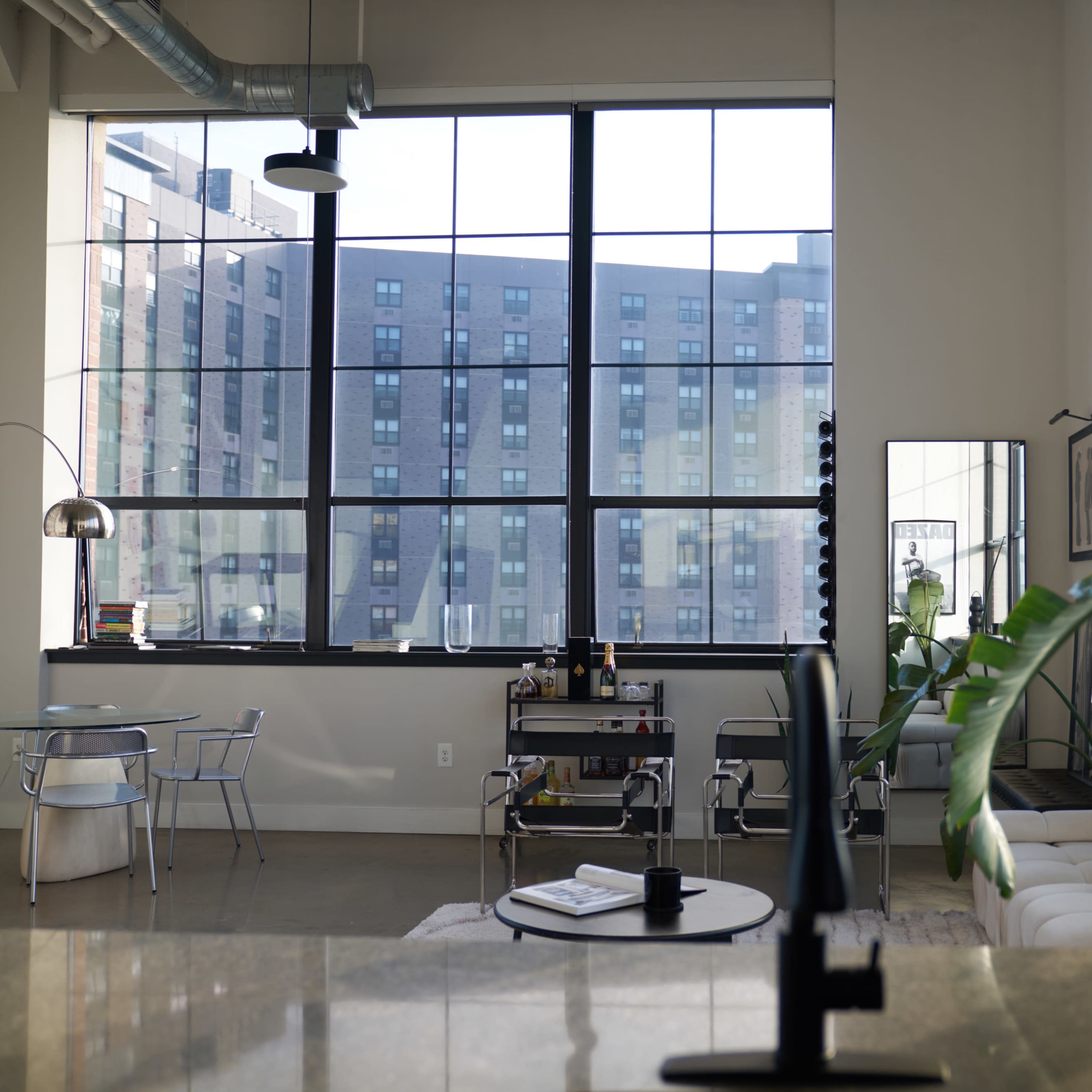 A modern interior space with large windows, a white sofa, a dining table set, and a plant, overlooking a city view.