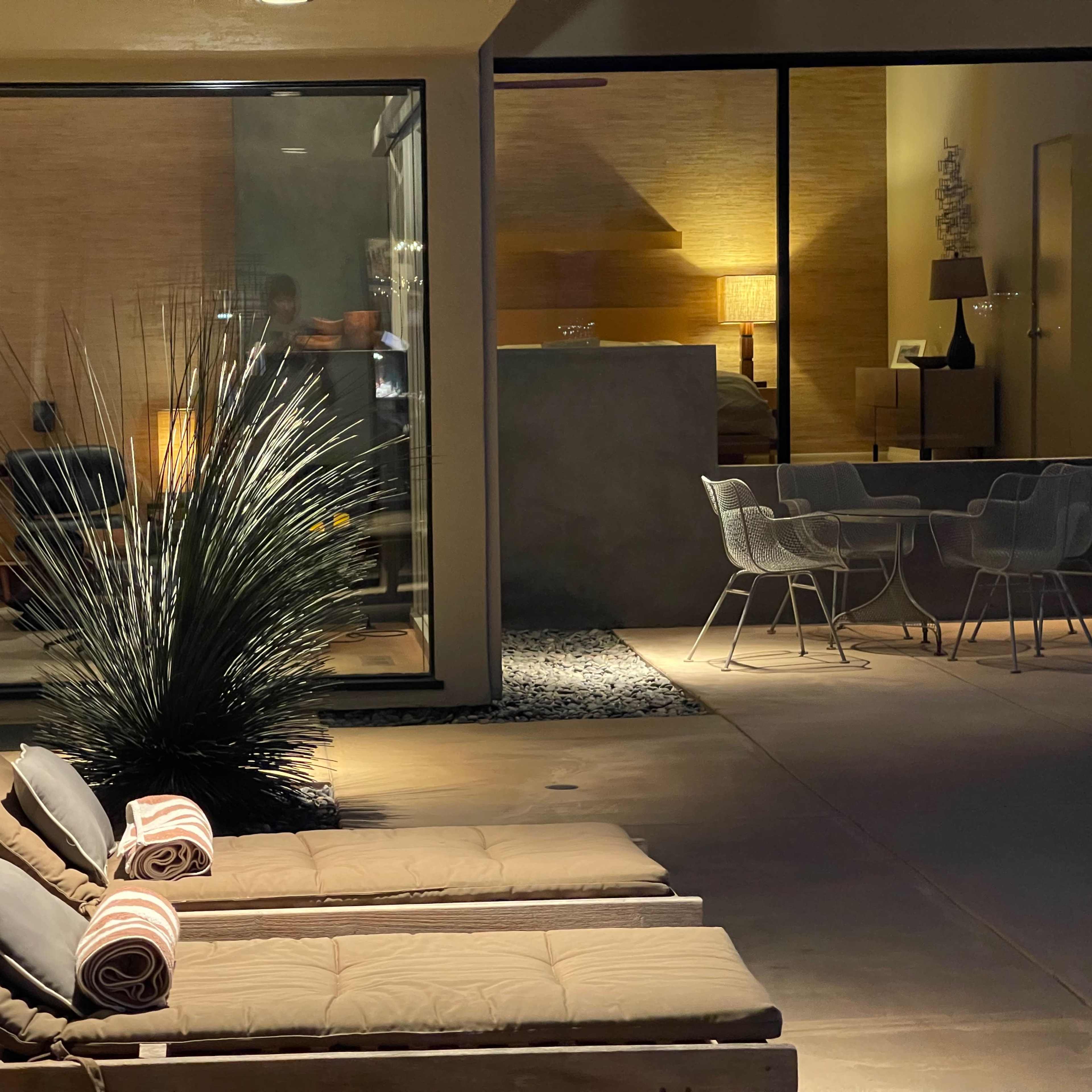 Two lounge chairs outside a modern glass-walled room, with a dining area visible in the background.