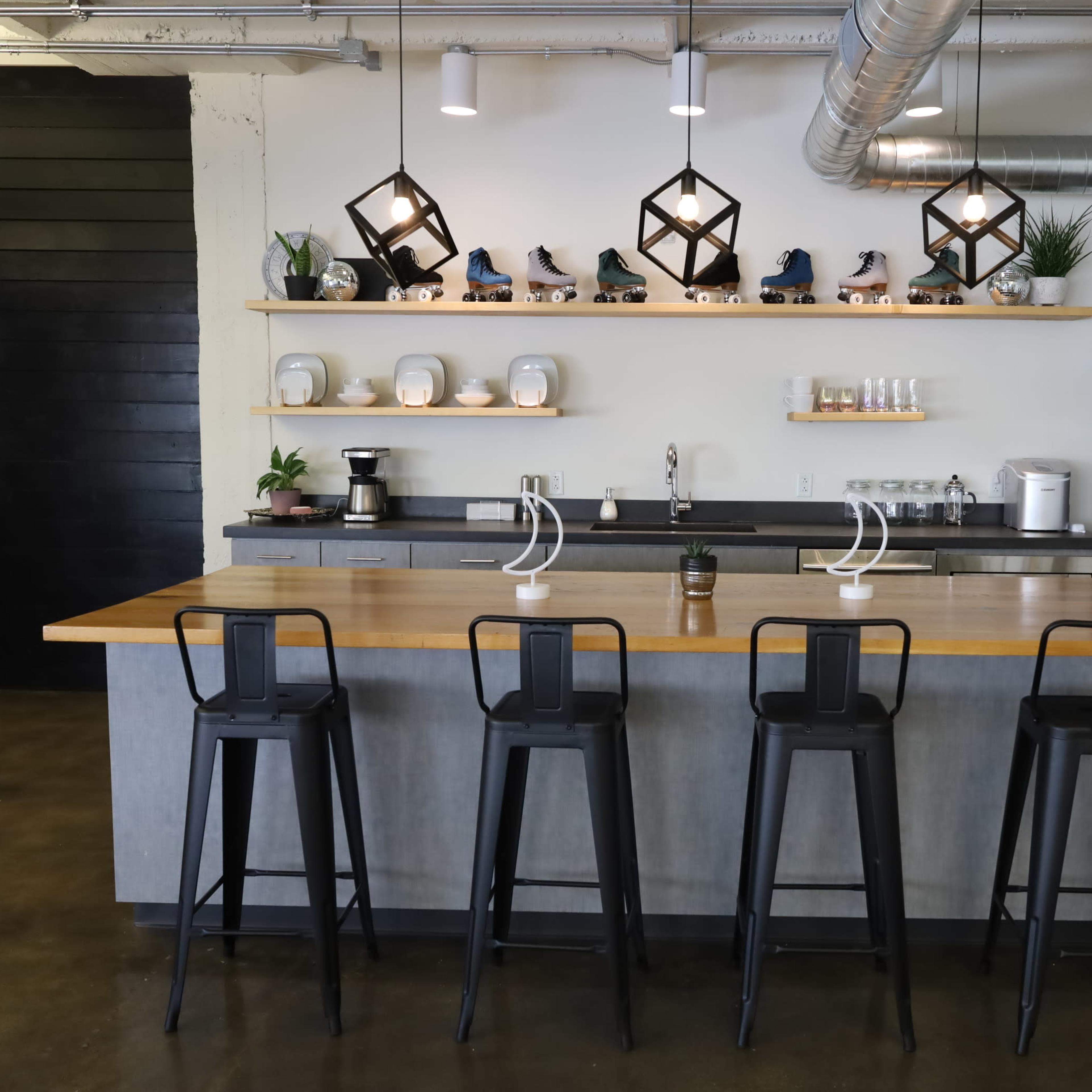 A modern kitchen features a gray island with bar stools, shelves displaying decorative items and roller skates, and a stainless steel refrigerator.