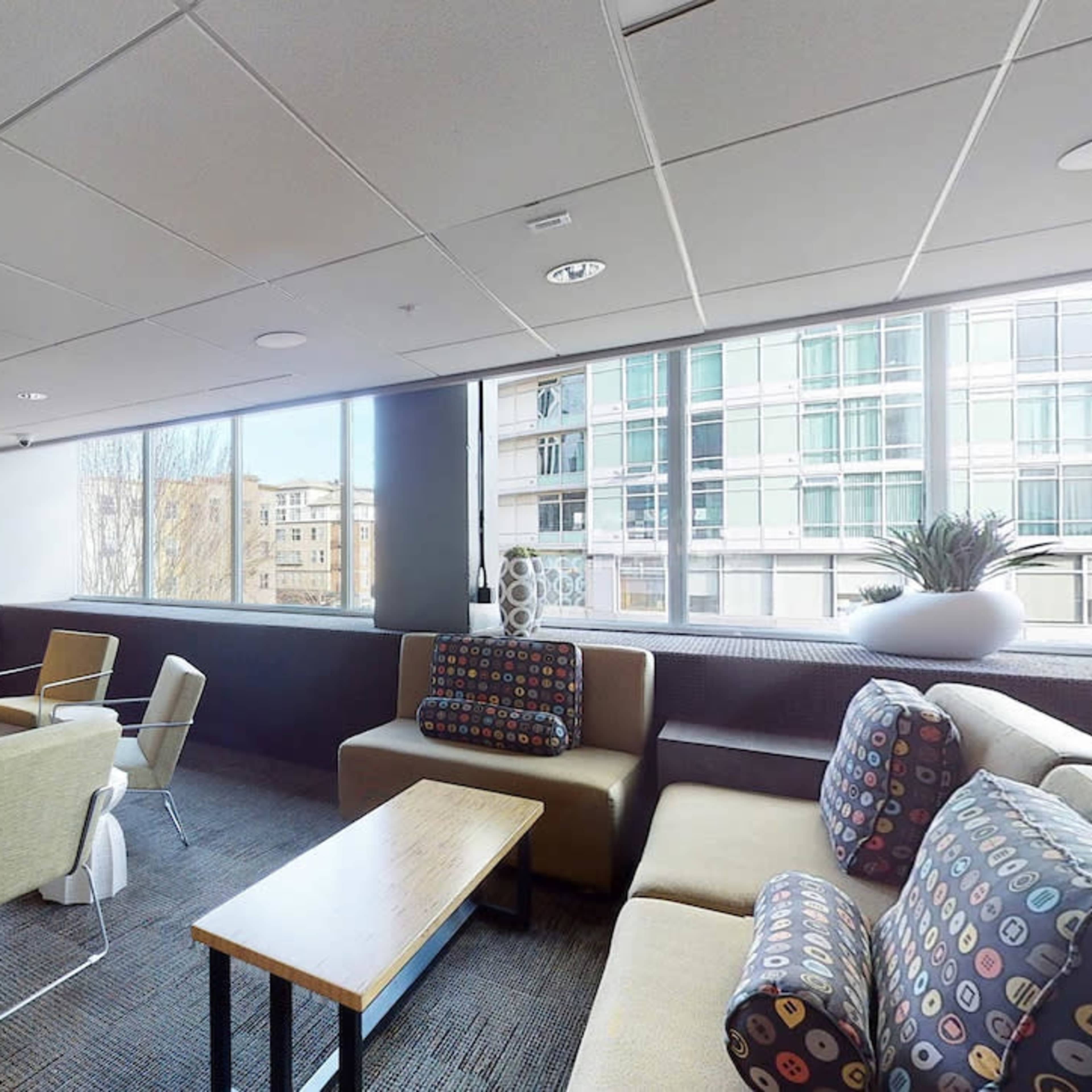 A modern lounge area with seating, a large television, and windows providing natural light.