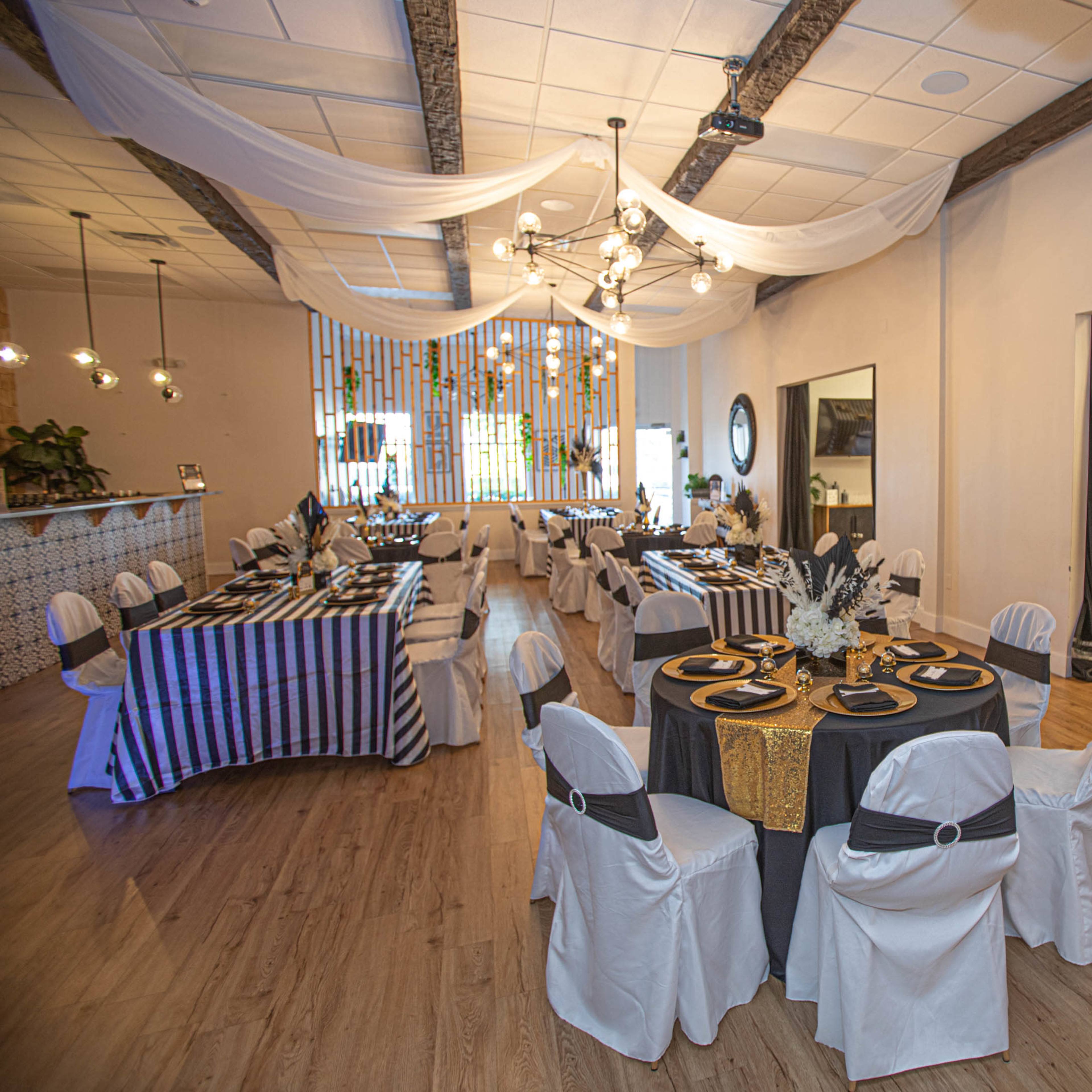 A banquet hall set up with tables covered in black and white striped and solid tablecloths, decorated with elegant table settings, and stylish balloon arrangements on one side.