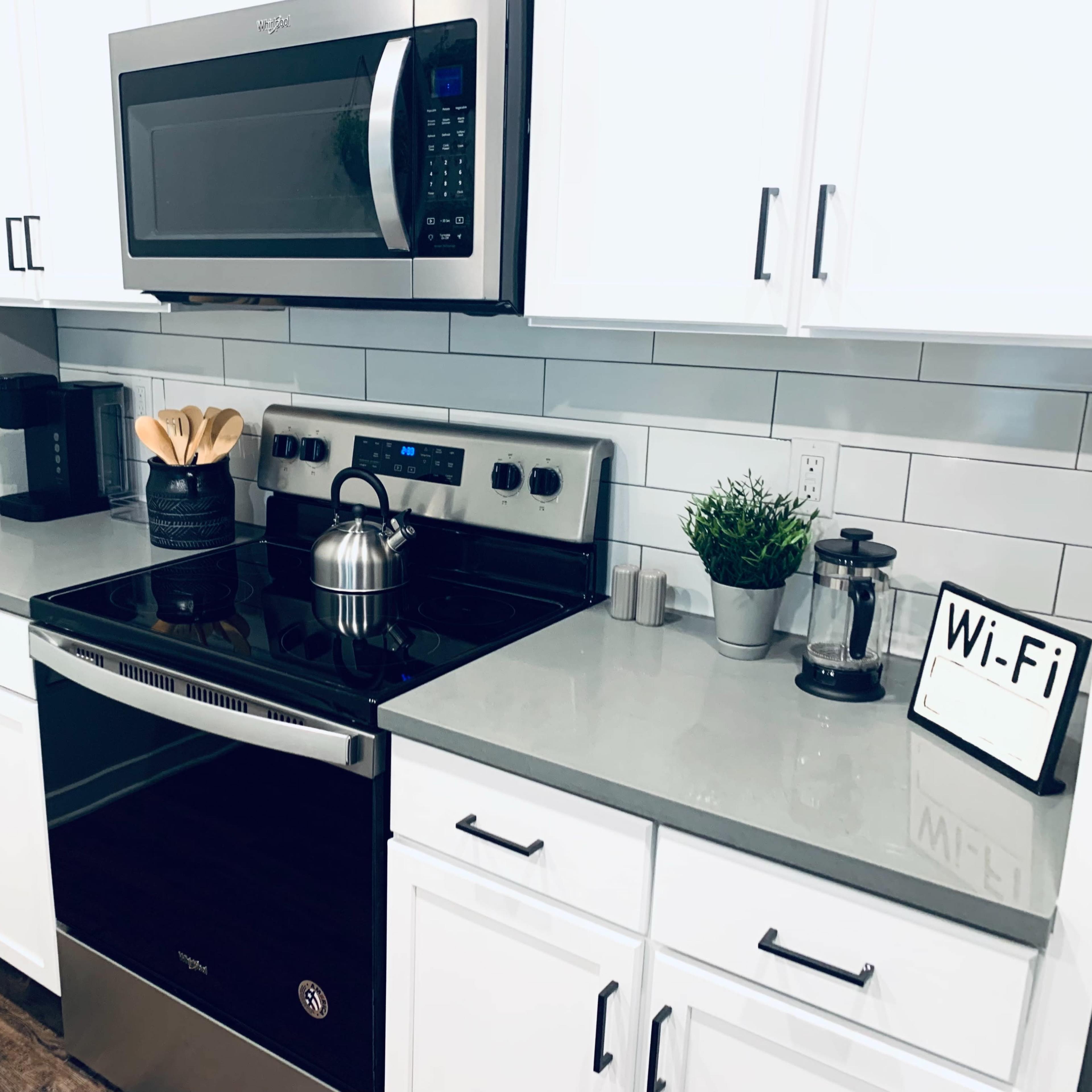 A modern kitchen features a black stove and microwave, white cabinets, a coffee maker, and a small plant on the countertop.