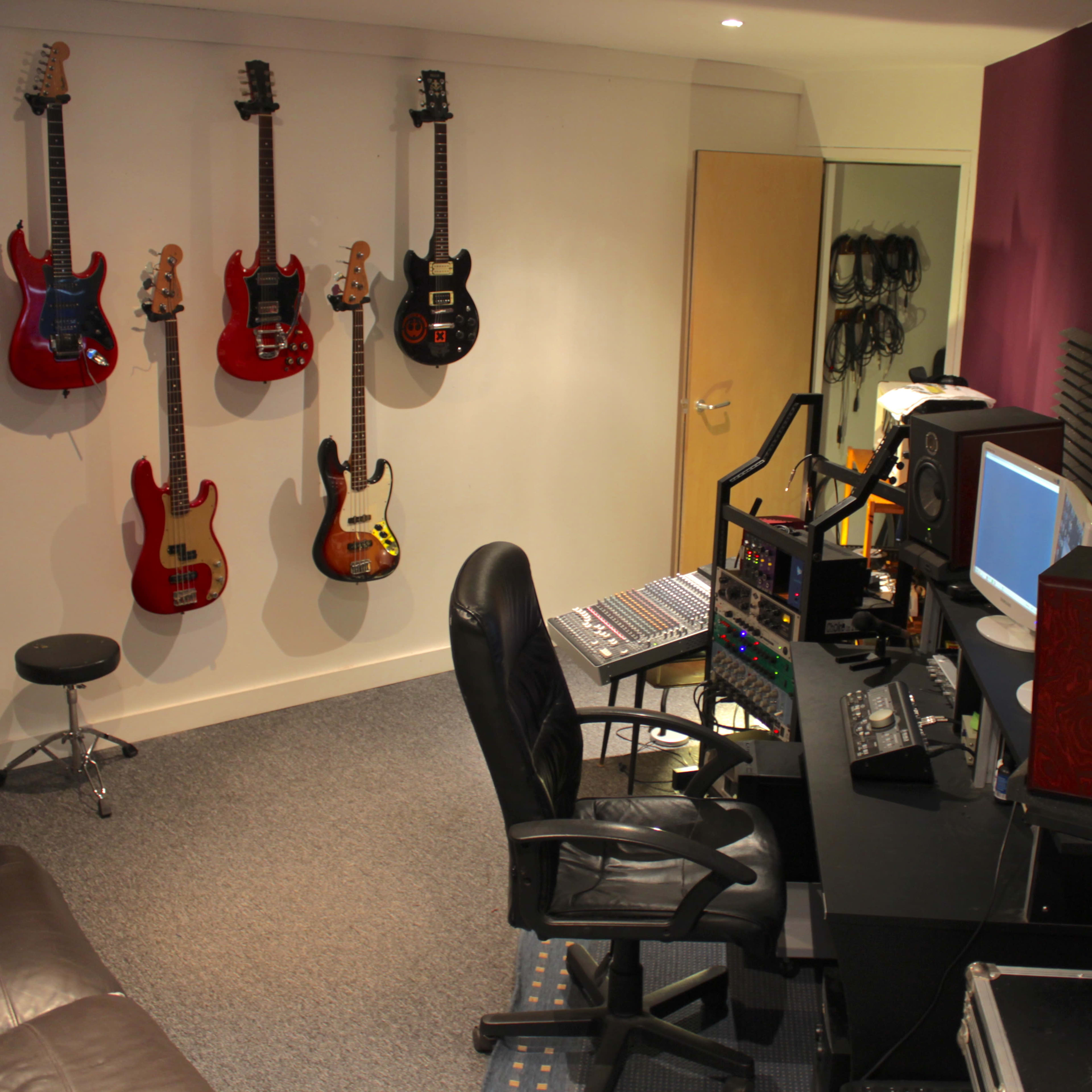 A music studio with a control desk, computer setup, and six electric guitars mounted on the wall.