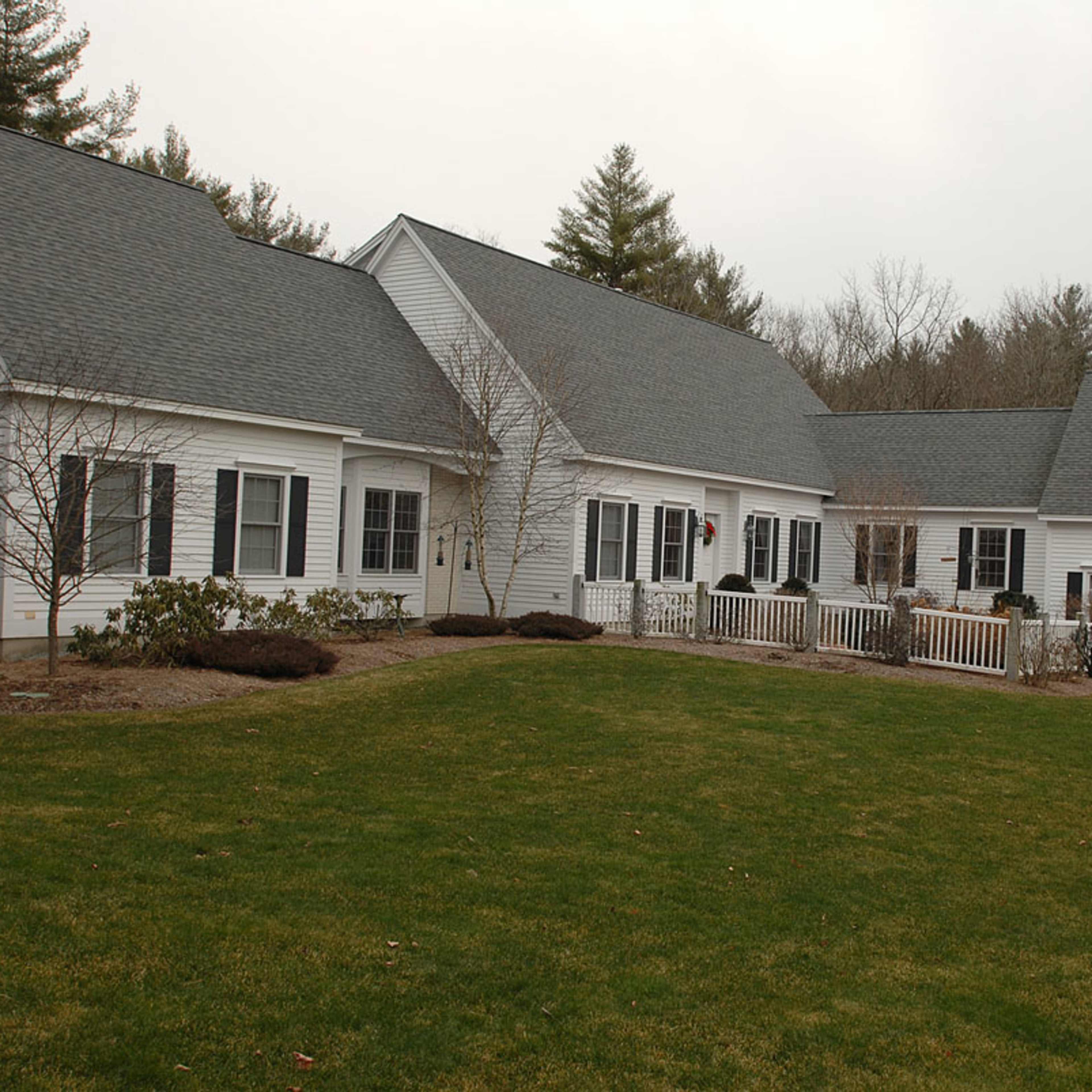 A large white house with multiple sections and a well-maintained lawn, surrounded by trees.