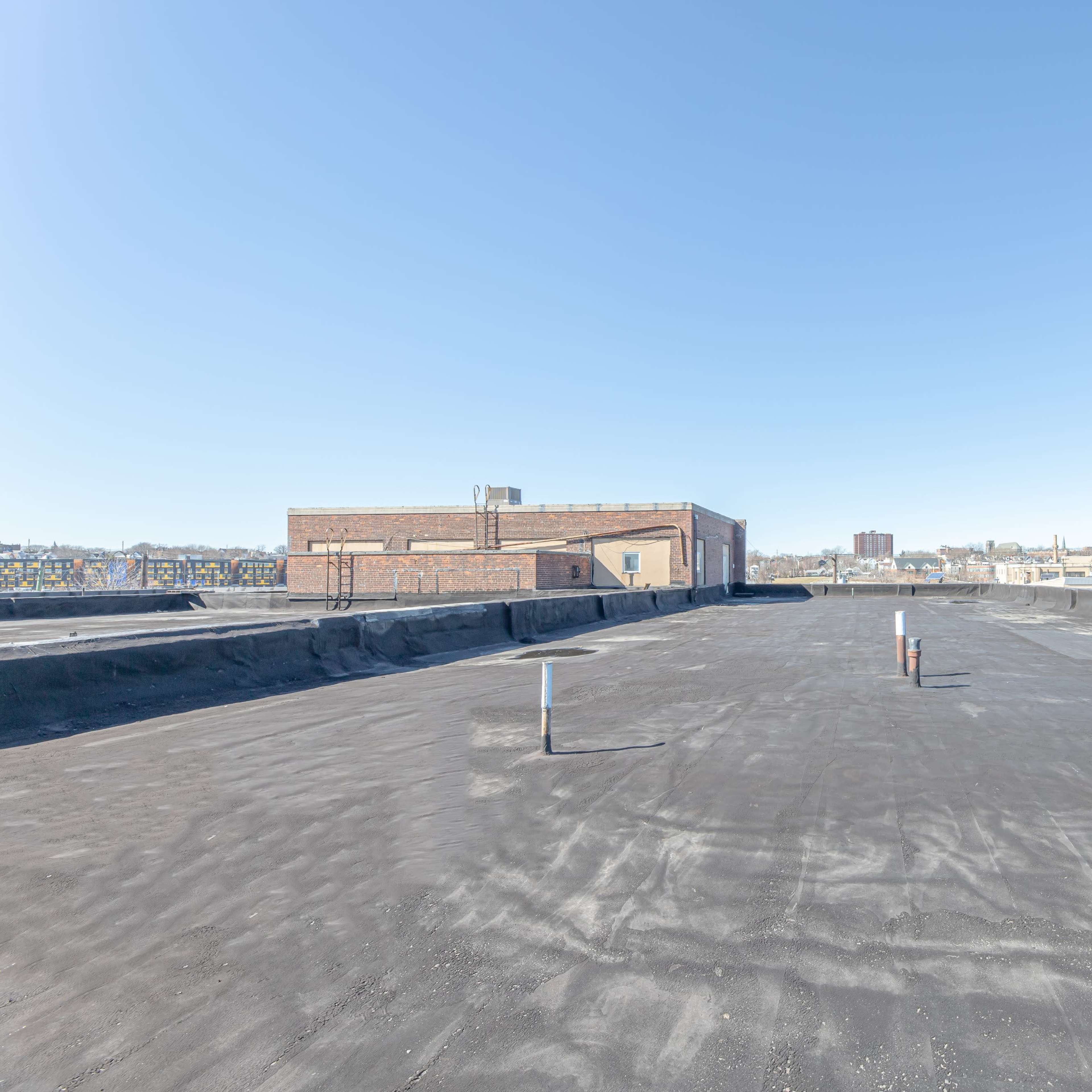 A flat rooftop with a black surface, two pipes protruding from it, and a clear blue sky in the background.