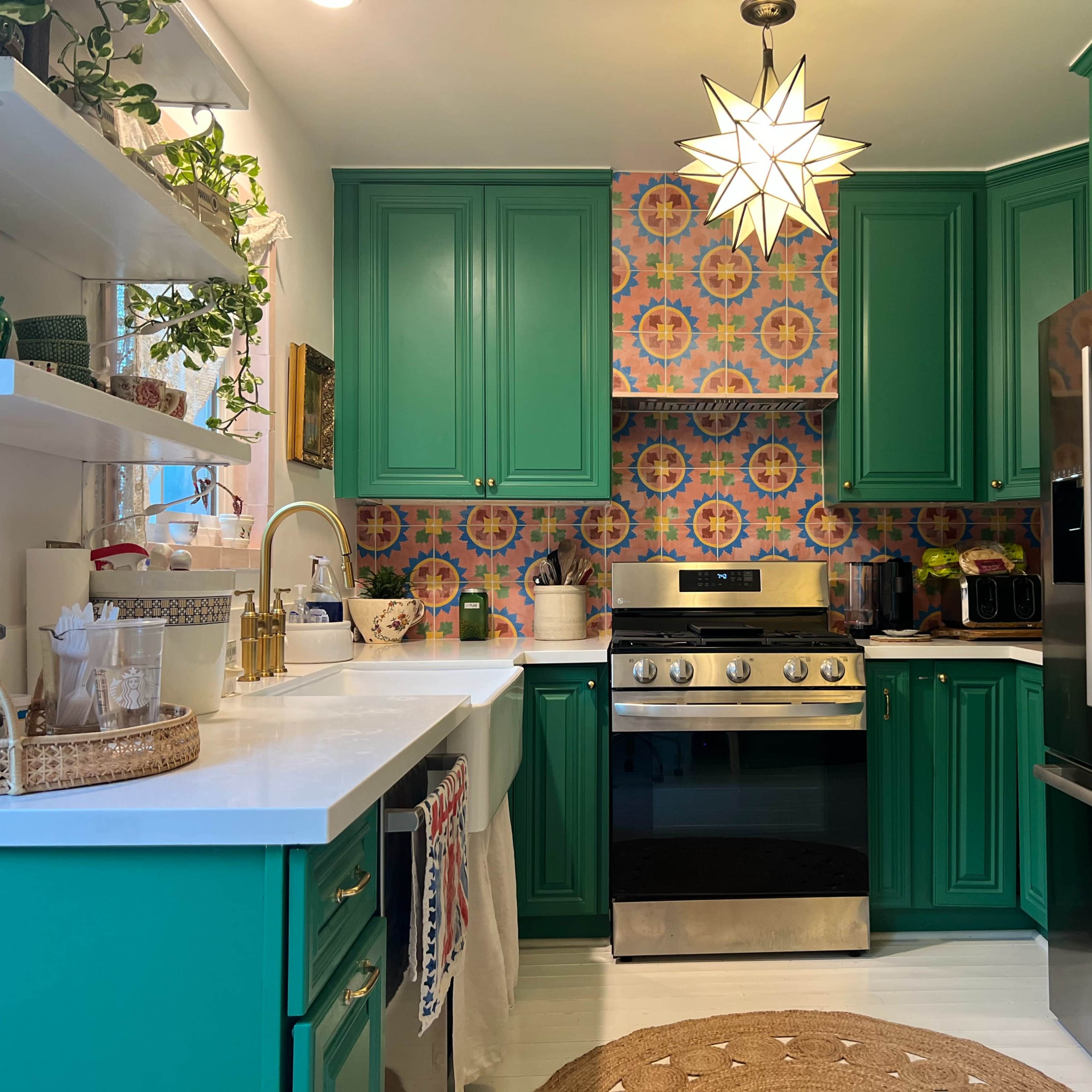 The kitchen features green cabinetry, a stainless steel stove, and patterned tile backsplash, with natural light coming through a window.