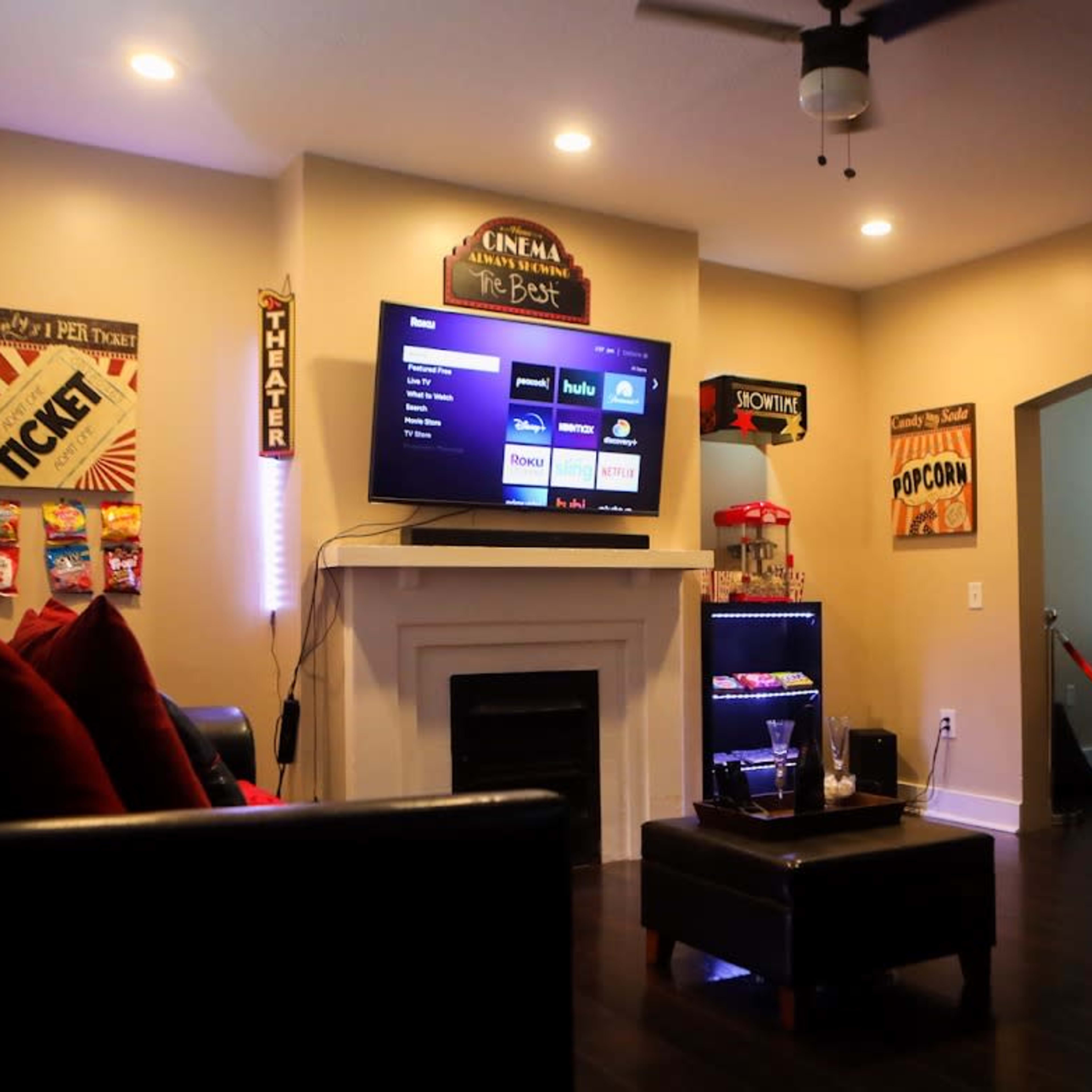 A cozy home theater setup with a white fireplace, a large TV displaying streaming options, and decor featuring popcorn and ticket themes on the walls.