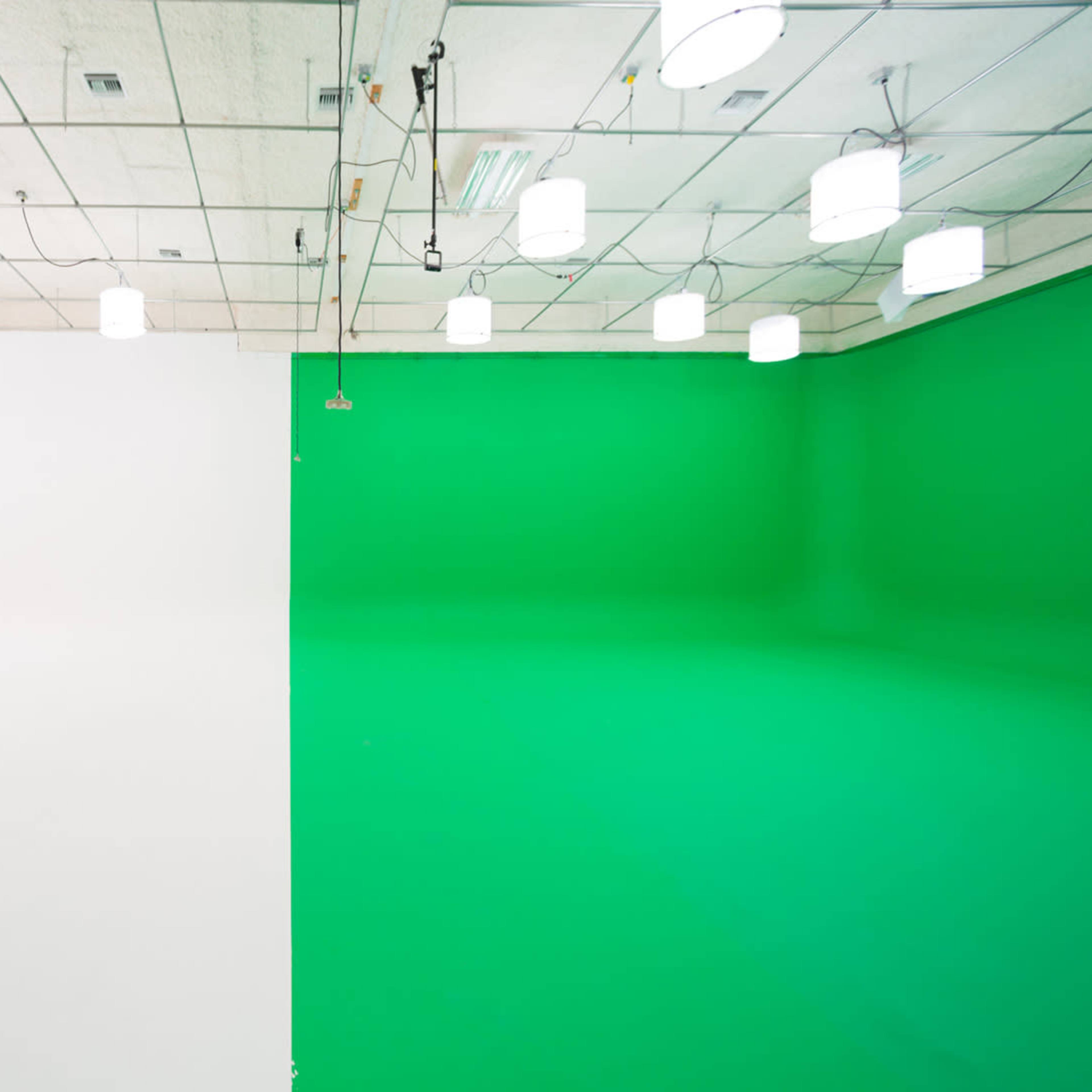 A studio space divided into two sections, one with a white wall and the other with a green wall, illuminated by overhead lights.