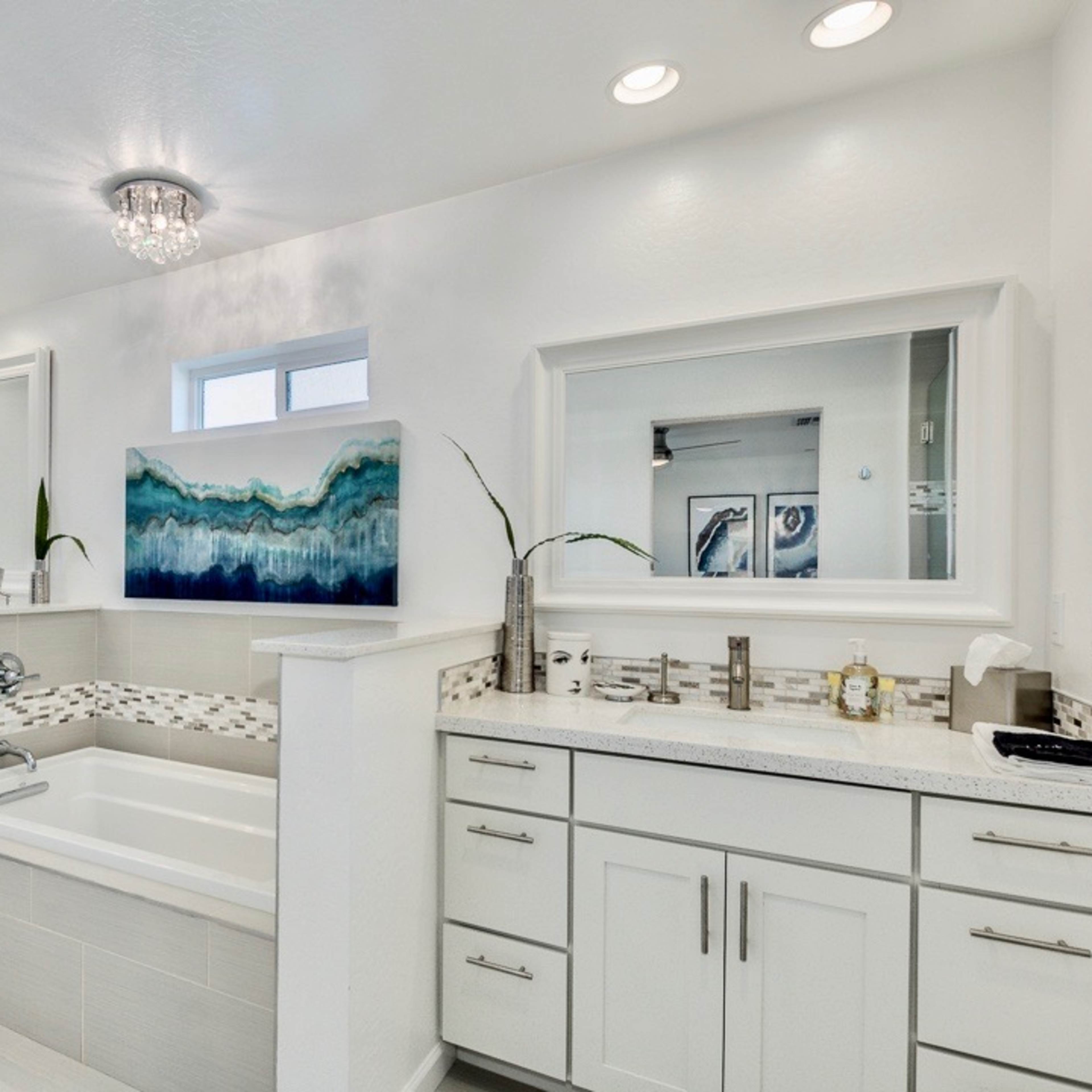 A modern bathroom featuring a bathtub, double sinks, and a large mirror, with decorative artwork and ample lighting.