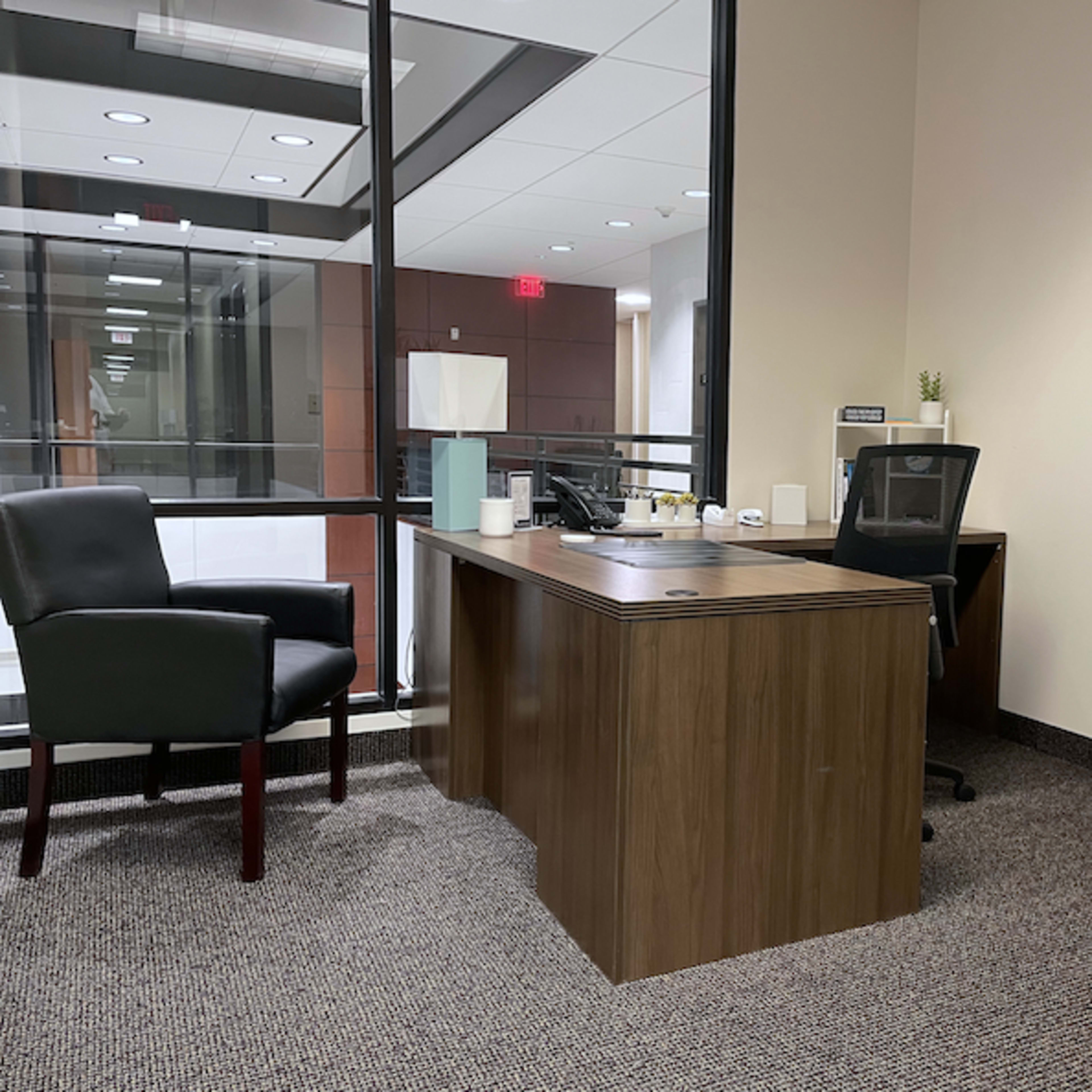 A modern office space featuring a wooden desk, a black chair, a phone, and a decorative painting on the wall.