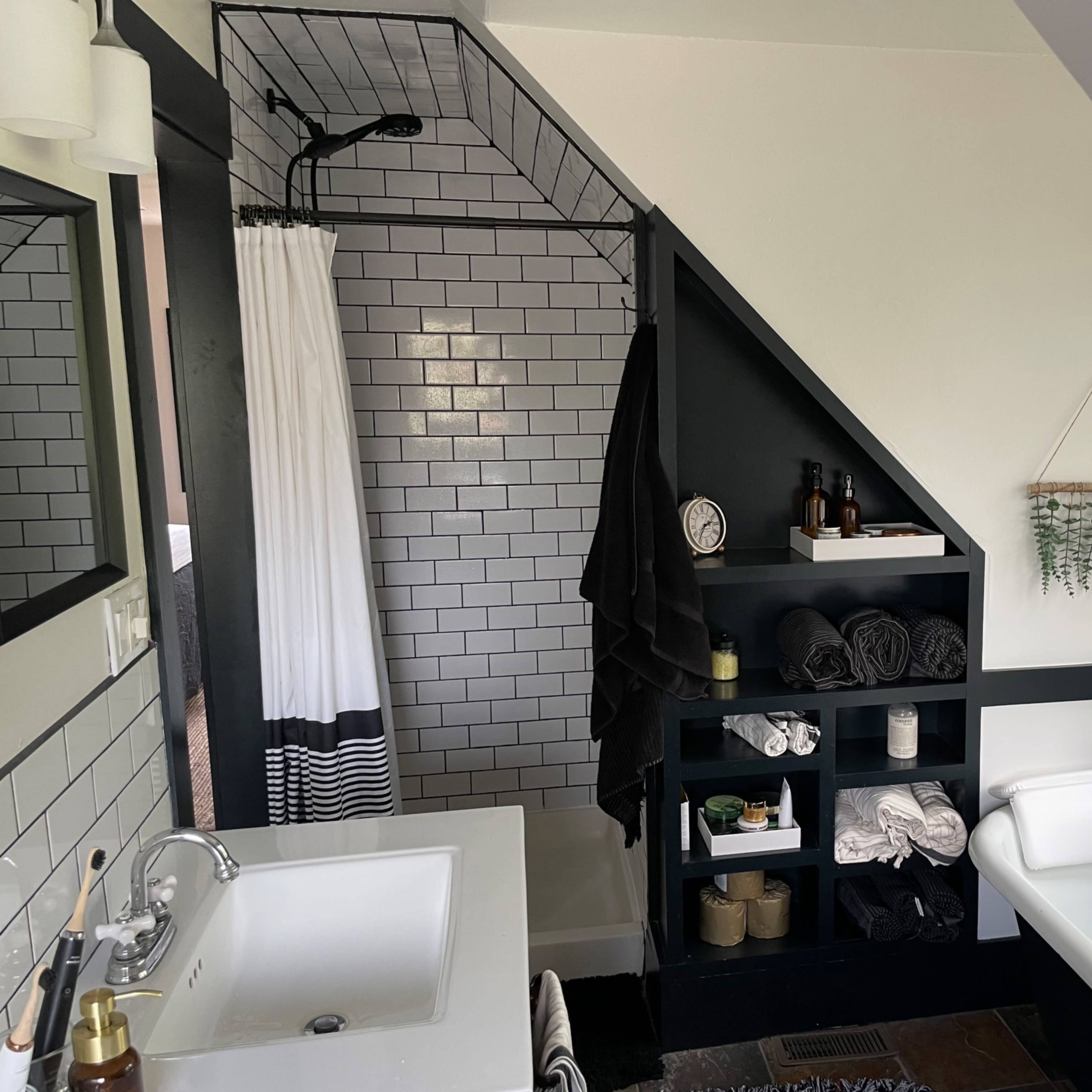 A modern bathroom featuring a walk-in shower with black tiles, a freestanding bathtub, and a shelf filled with neatly arranged towels and toiletries.
