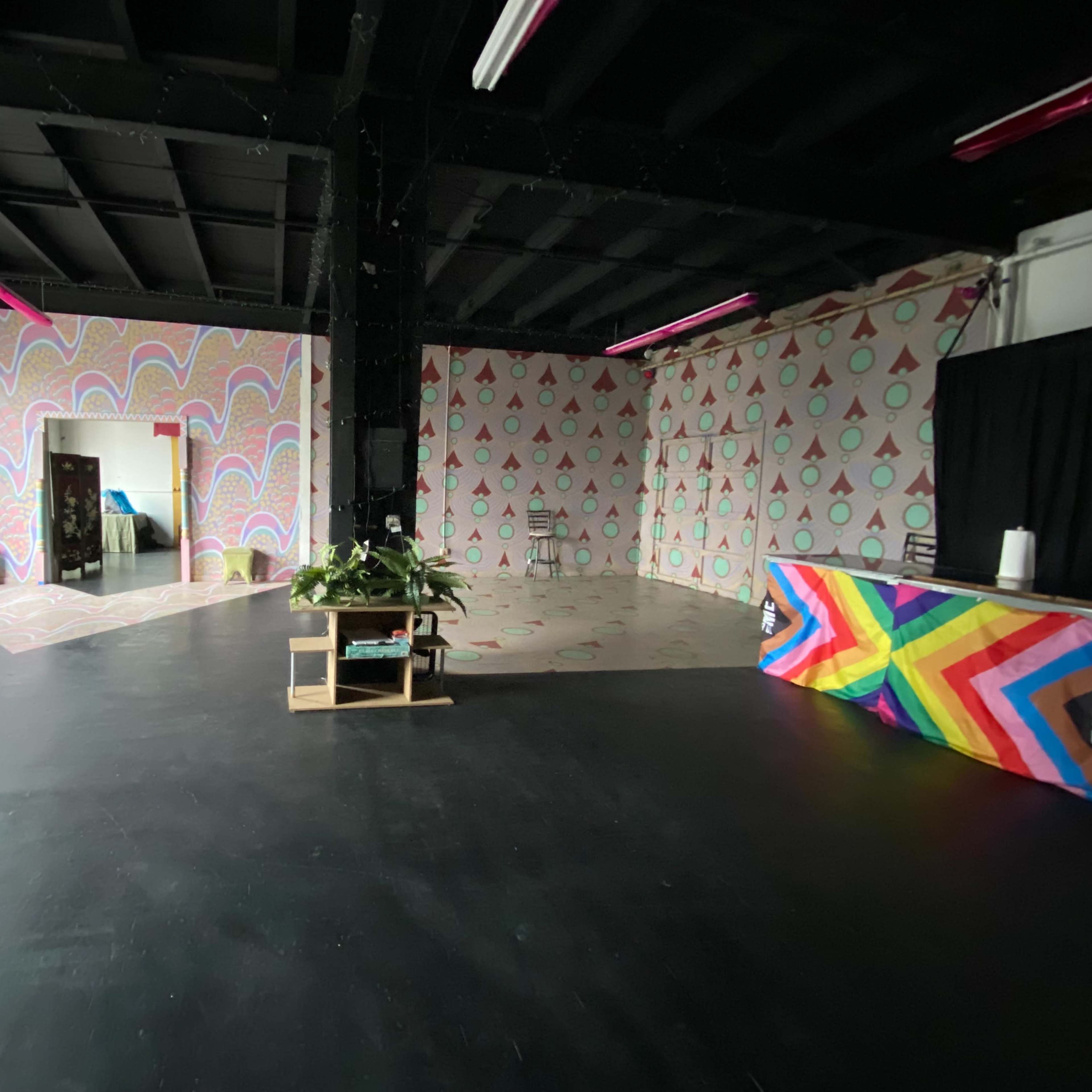 A spacious room with colorful patterned walls, a dark floor, and a small stage area with a vibrant rainbow backdrop.