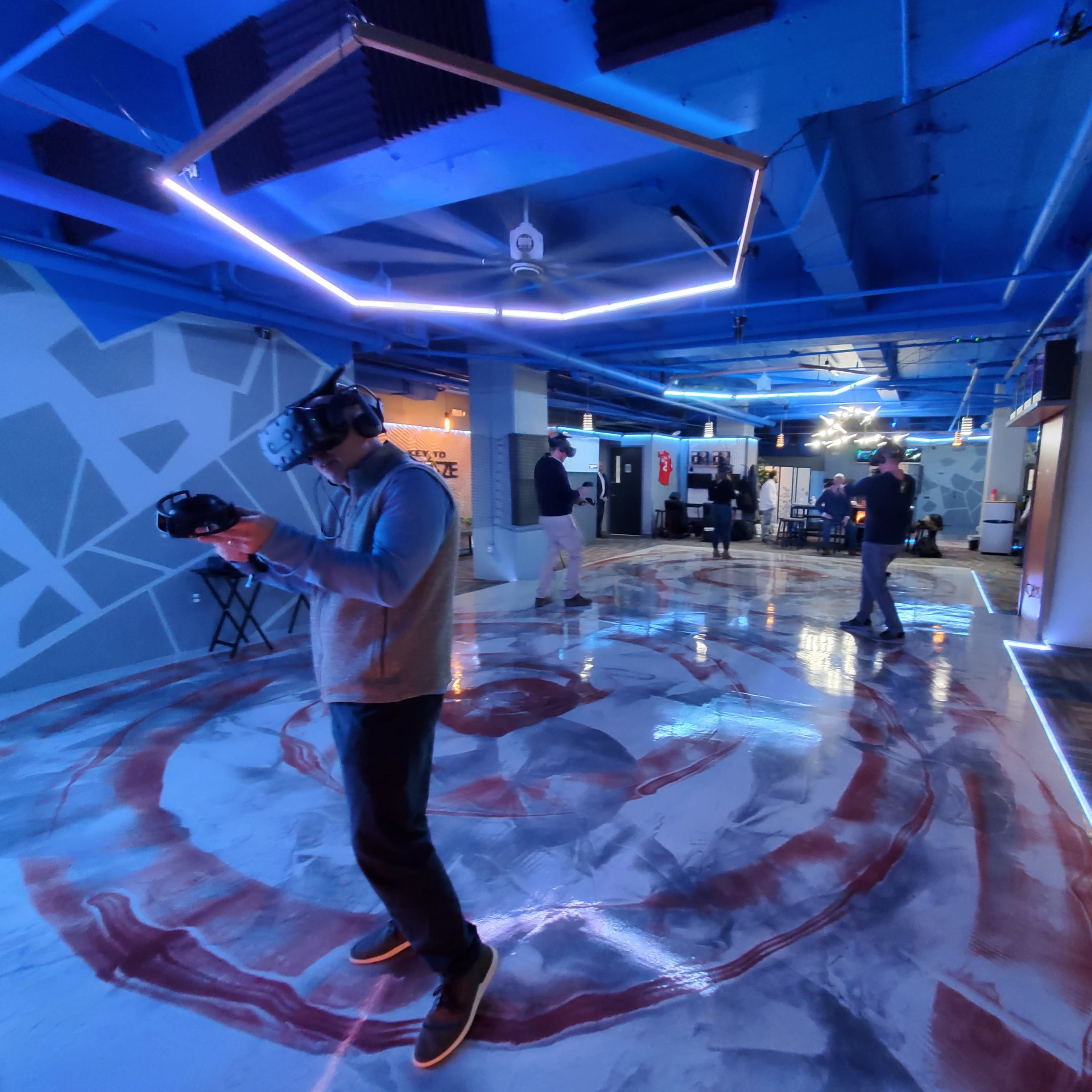 A group of people experiences virtual reality in a modern, blue-lit space with a uniquely designed floor.