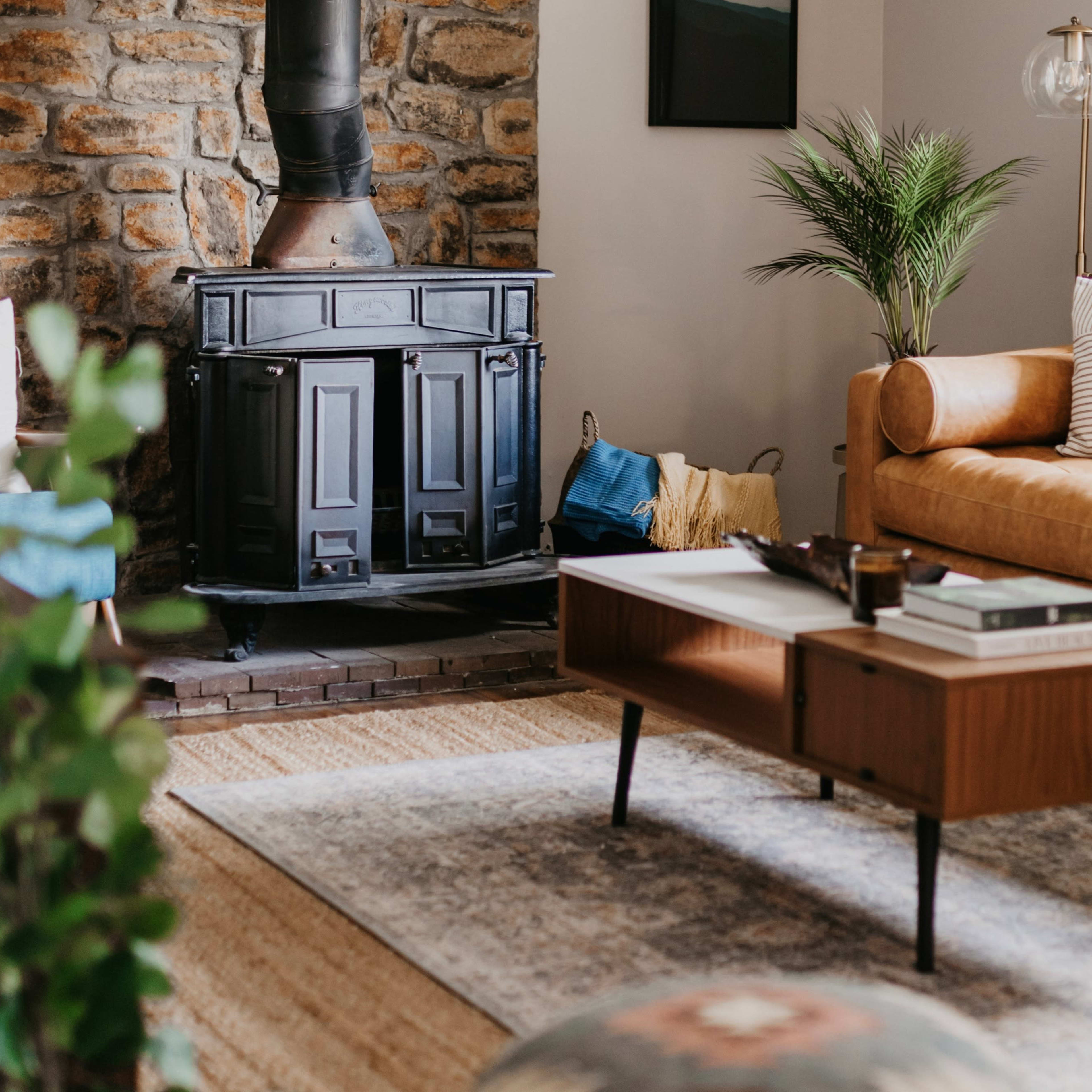 A cozy living room features a leather sofa, a wooden coffee table, and a stone fireplace with a metal stove.