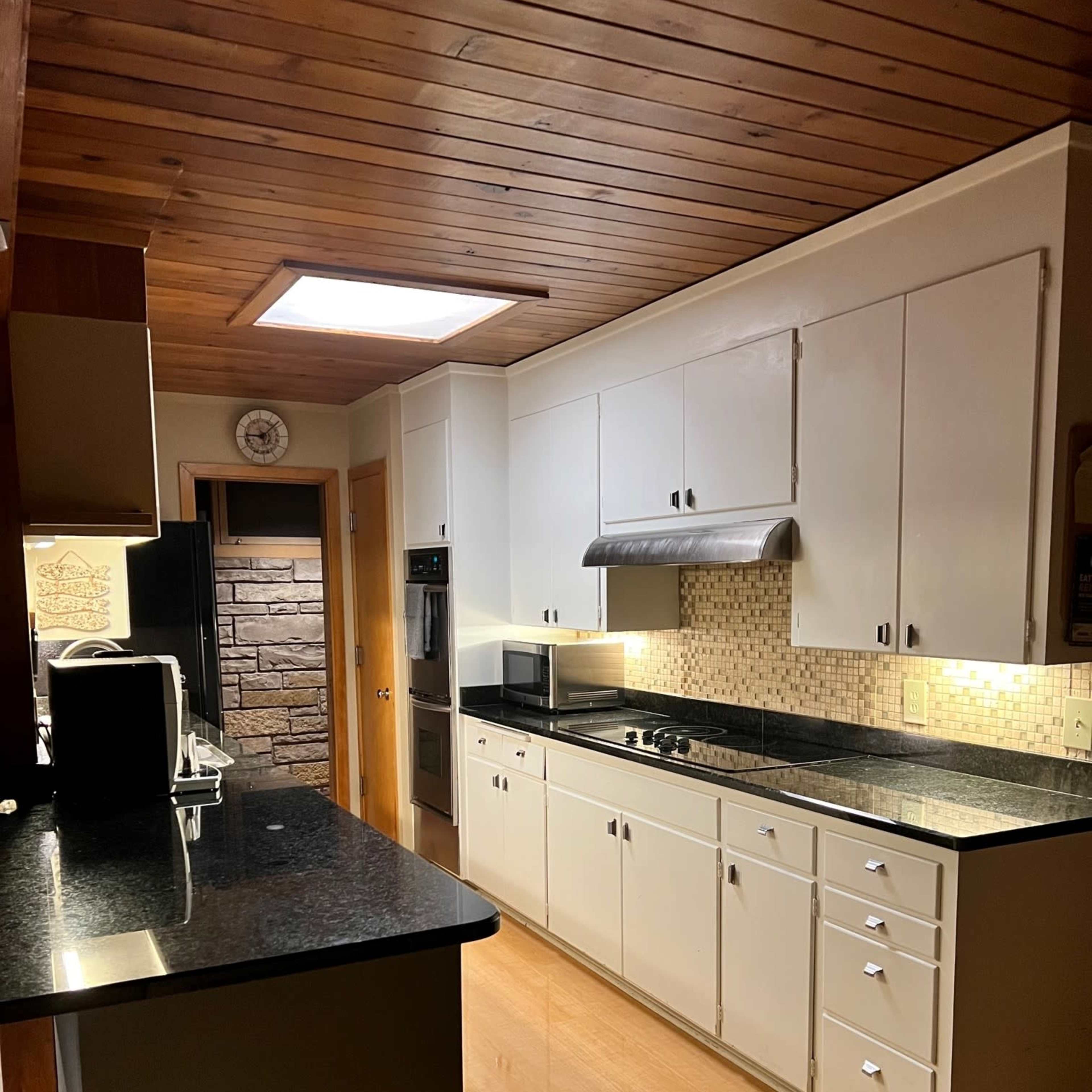 A bright kitchen with white cabinetry, a black countertop, and a skylight above.