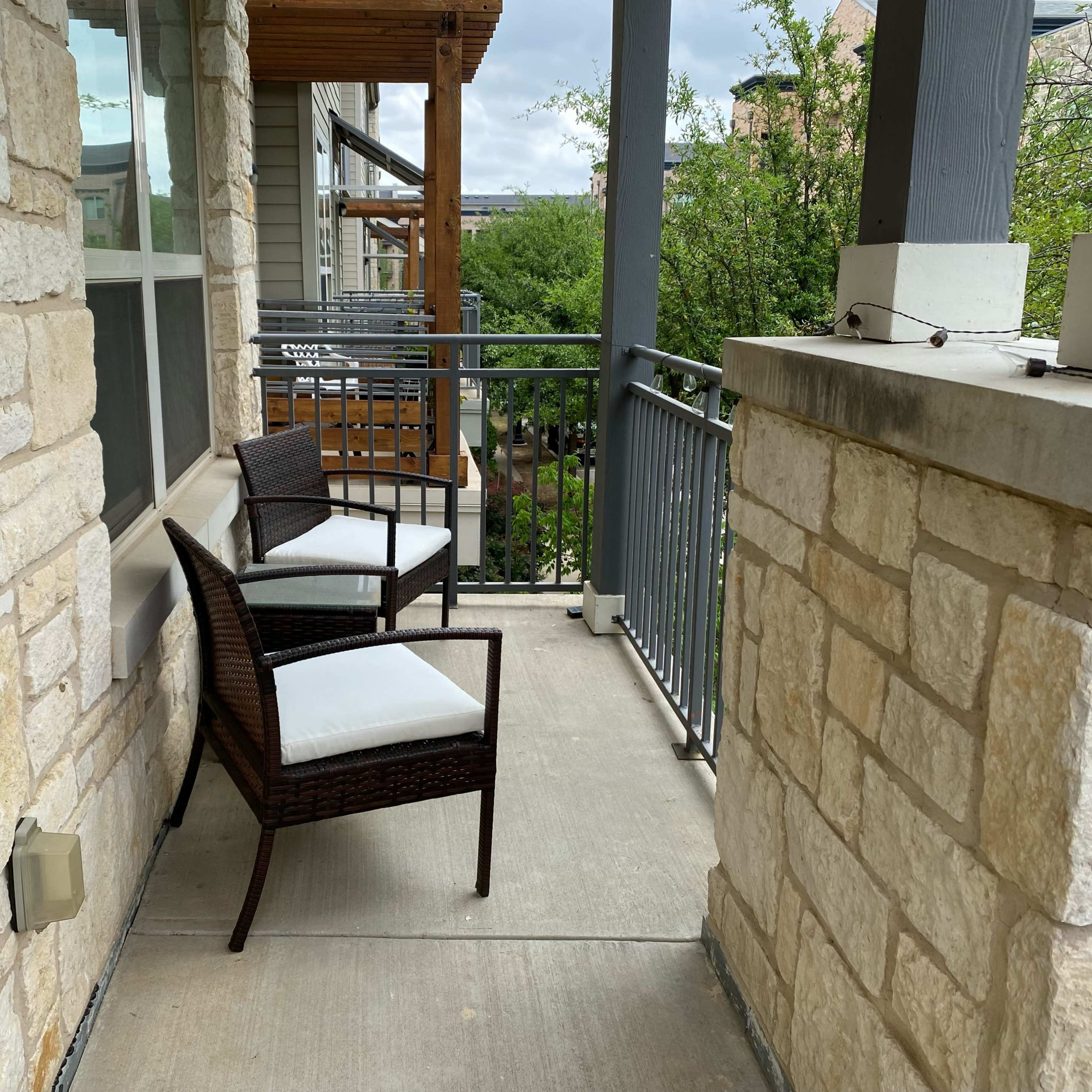 A small balcony with two chairs positioned against a stone wall, overlooking a green area.