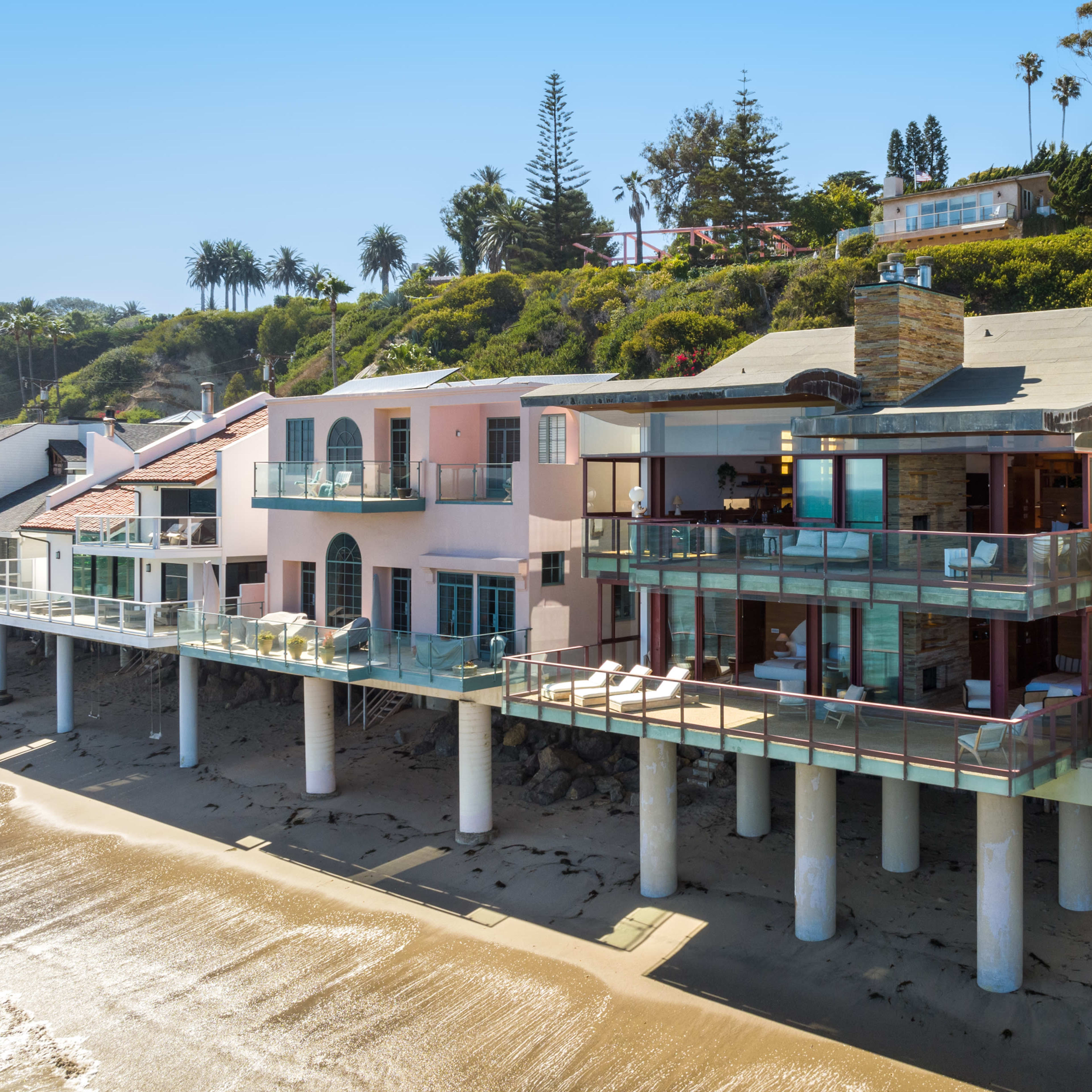 A row of modern beachfront homes with balconies elevated above the sandy shore.