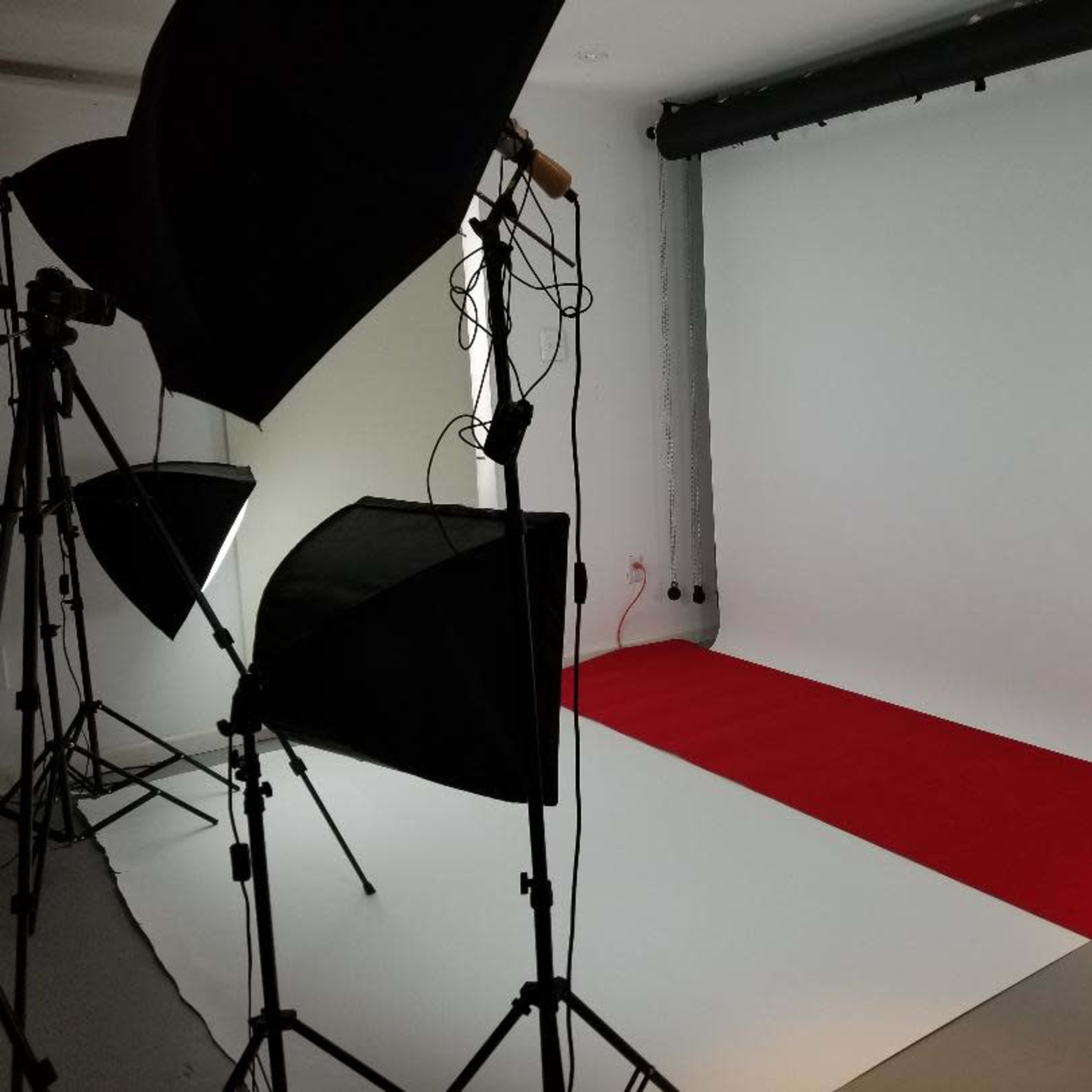 A photography studio with a red carpet, white backdrop, and several lighting setups on stands.