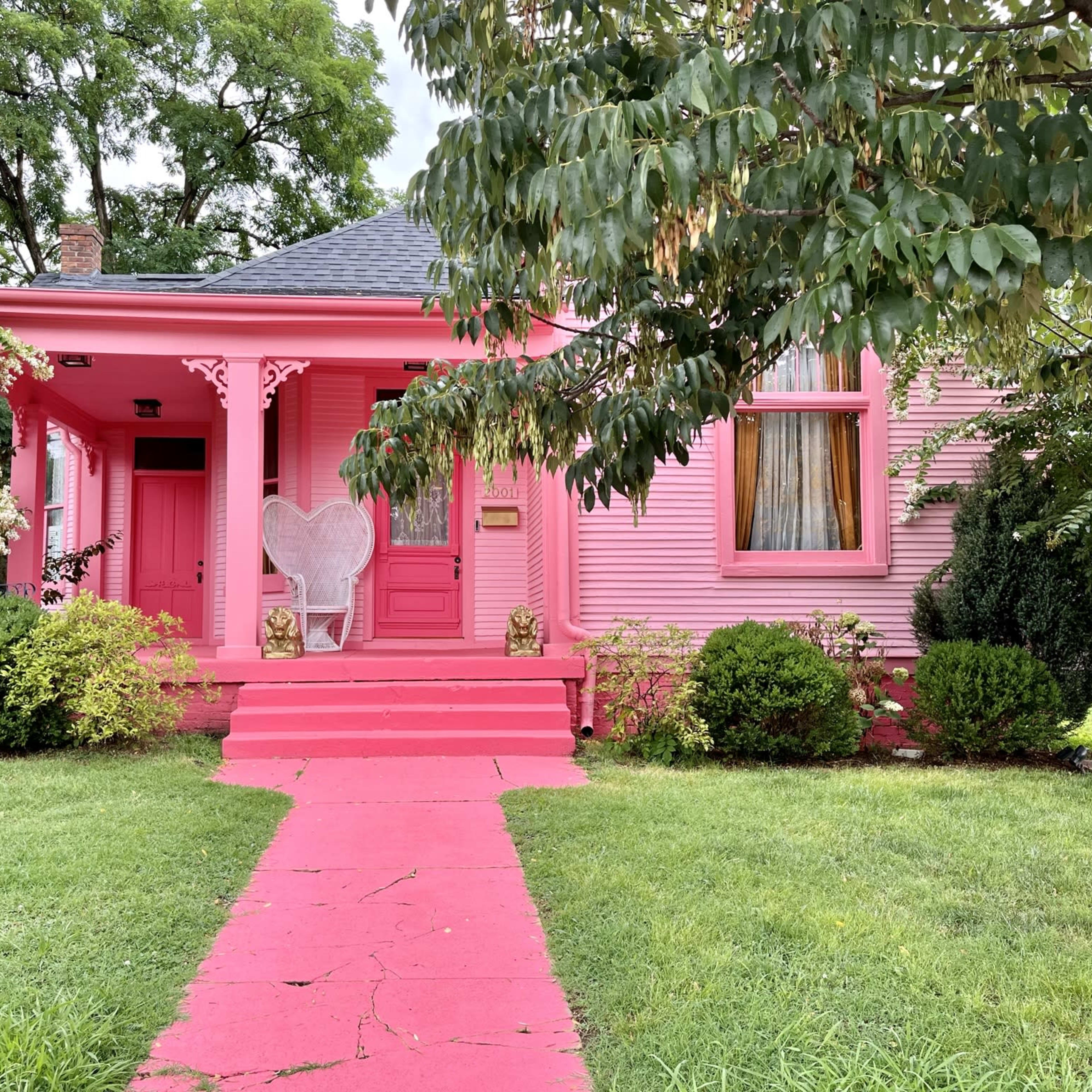 A pink house features a heart-shaped chair on the porch, with a bright pink pathway leading to it.
