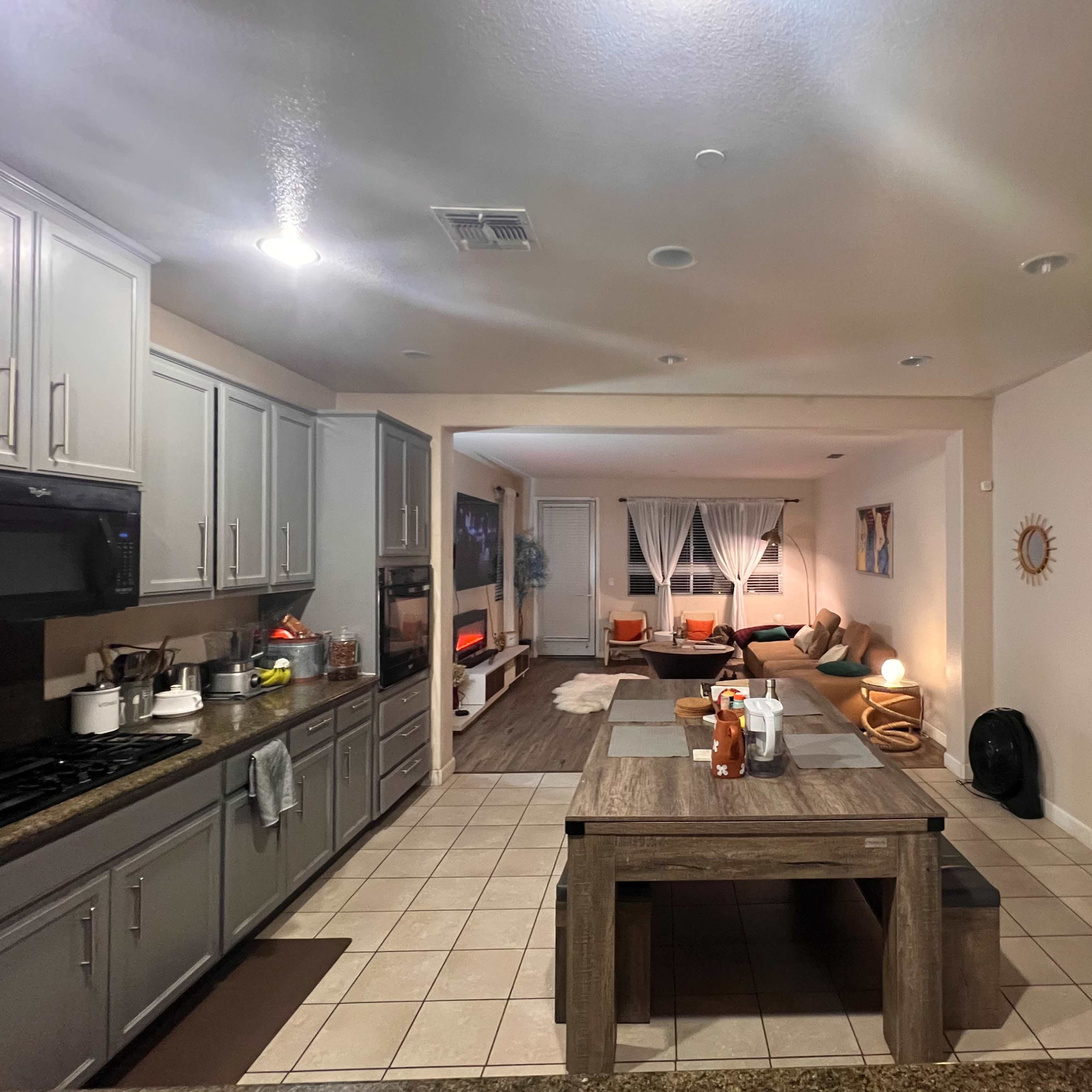 A spacious kitchen with gray cabinets and countertops, leading into a living area furnished with a couch and a coffee table.