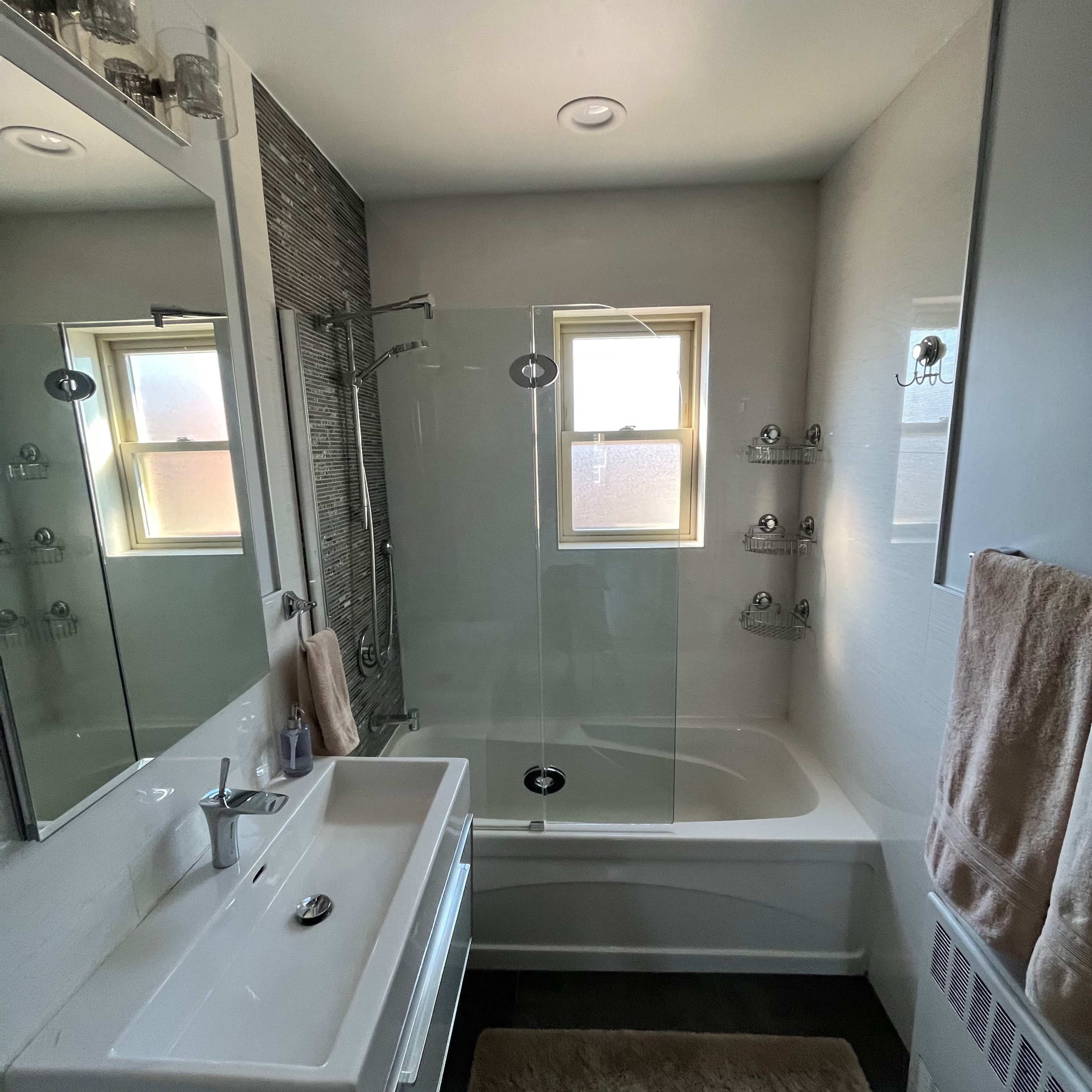 A modern bathroom featuring a glass shower enclosure, a bathtub, a wall-mounted sink with a mirror, and several shelves for toiletries.