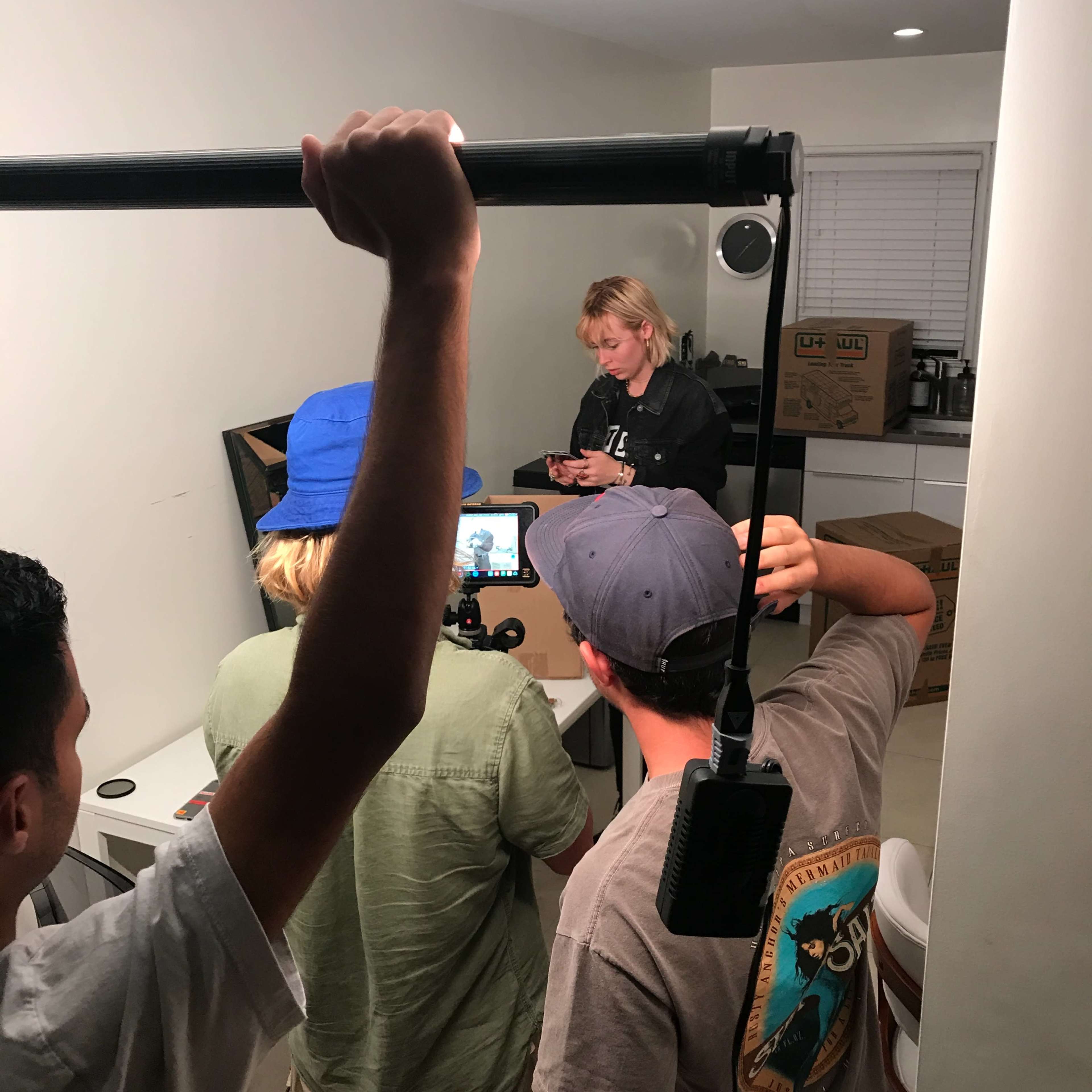 A group of four people is filming in a small room, focused on a laptop screen while one person holds a camera stabilizer.