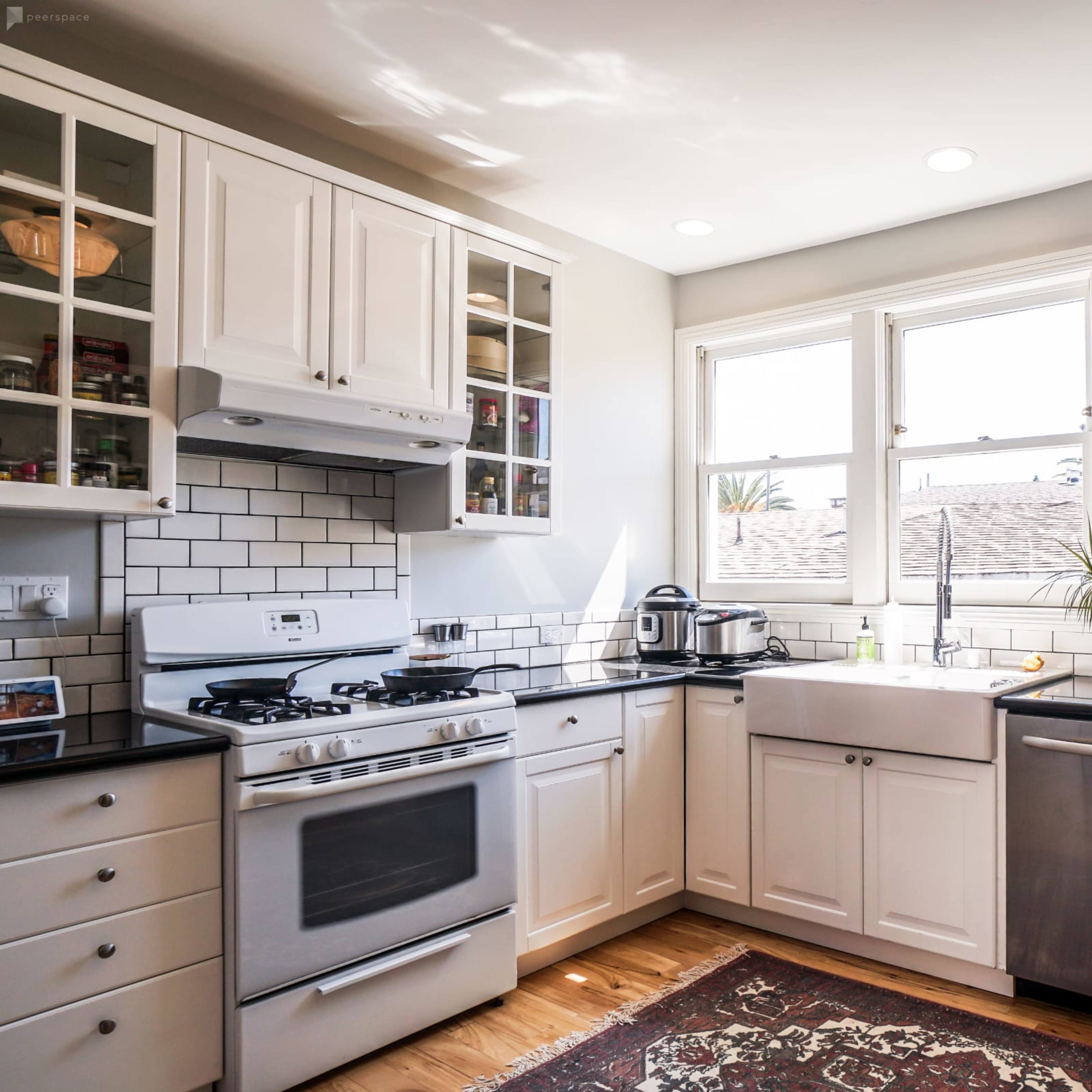 A modern kitchen features white cabinets, a large sink in front of windows, and stainless steel appliances on black countertops.