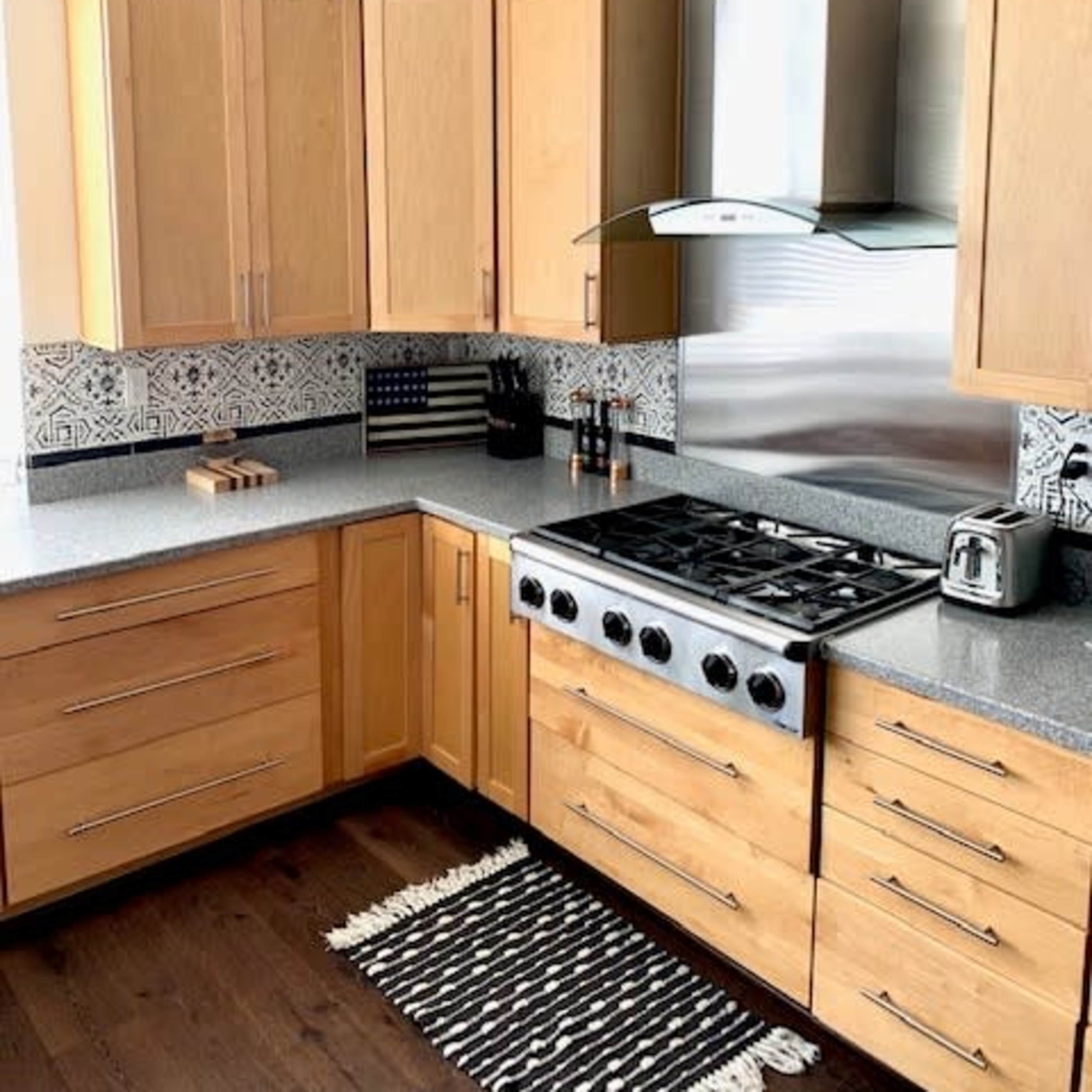 A modern kitchen features wooden cabinetry, a stainless steel range hood above a gas stove, and a patterned backsplash.