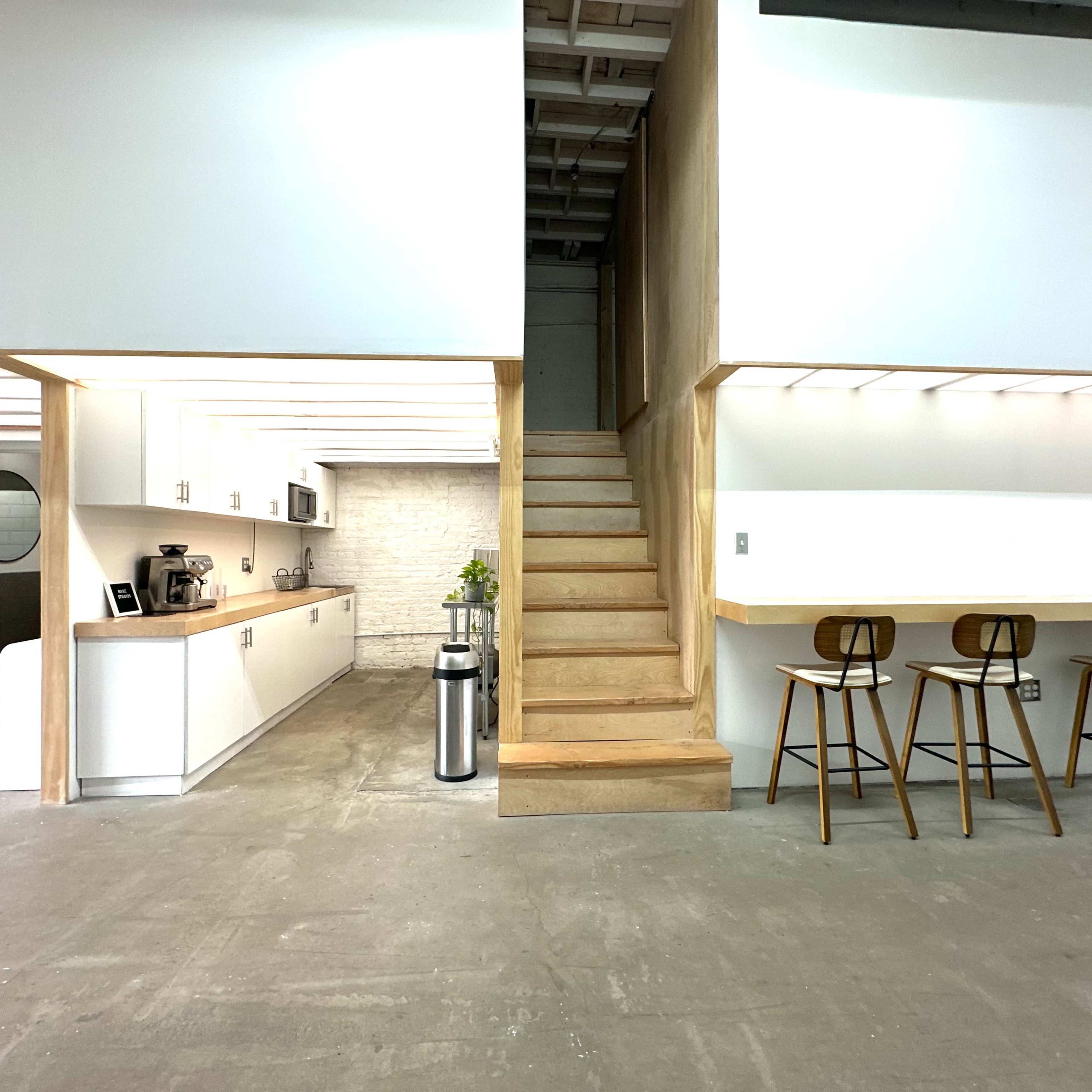 A modern kitchen with white cabinetry, a staircase leading to an upper level, and wooden bar stools next to a counter.