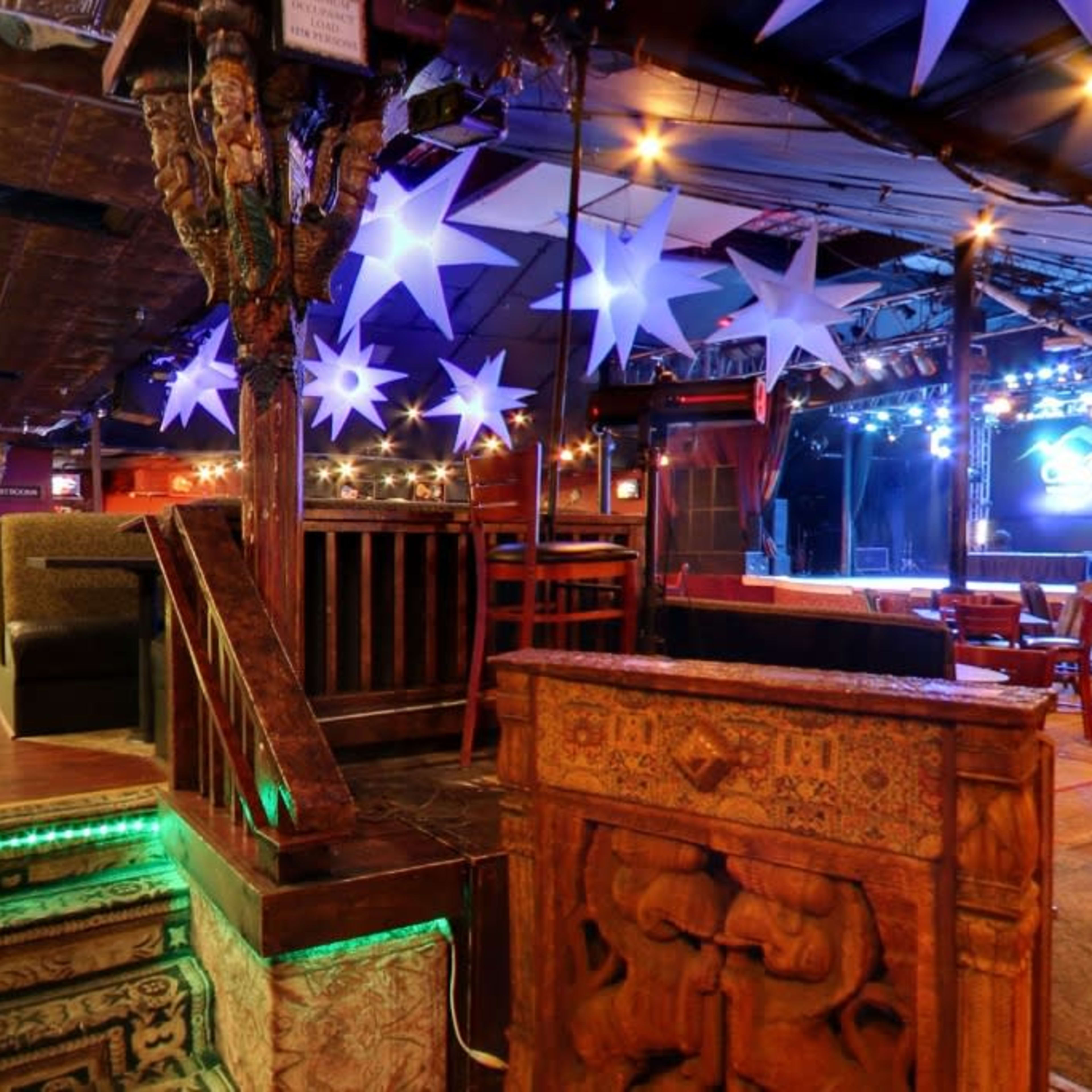 The interior of a vibrant live music venue features a stage with blue lights, colorful decor, and a mix of seating arrangements.