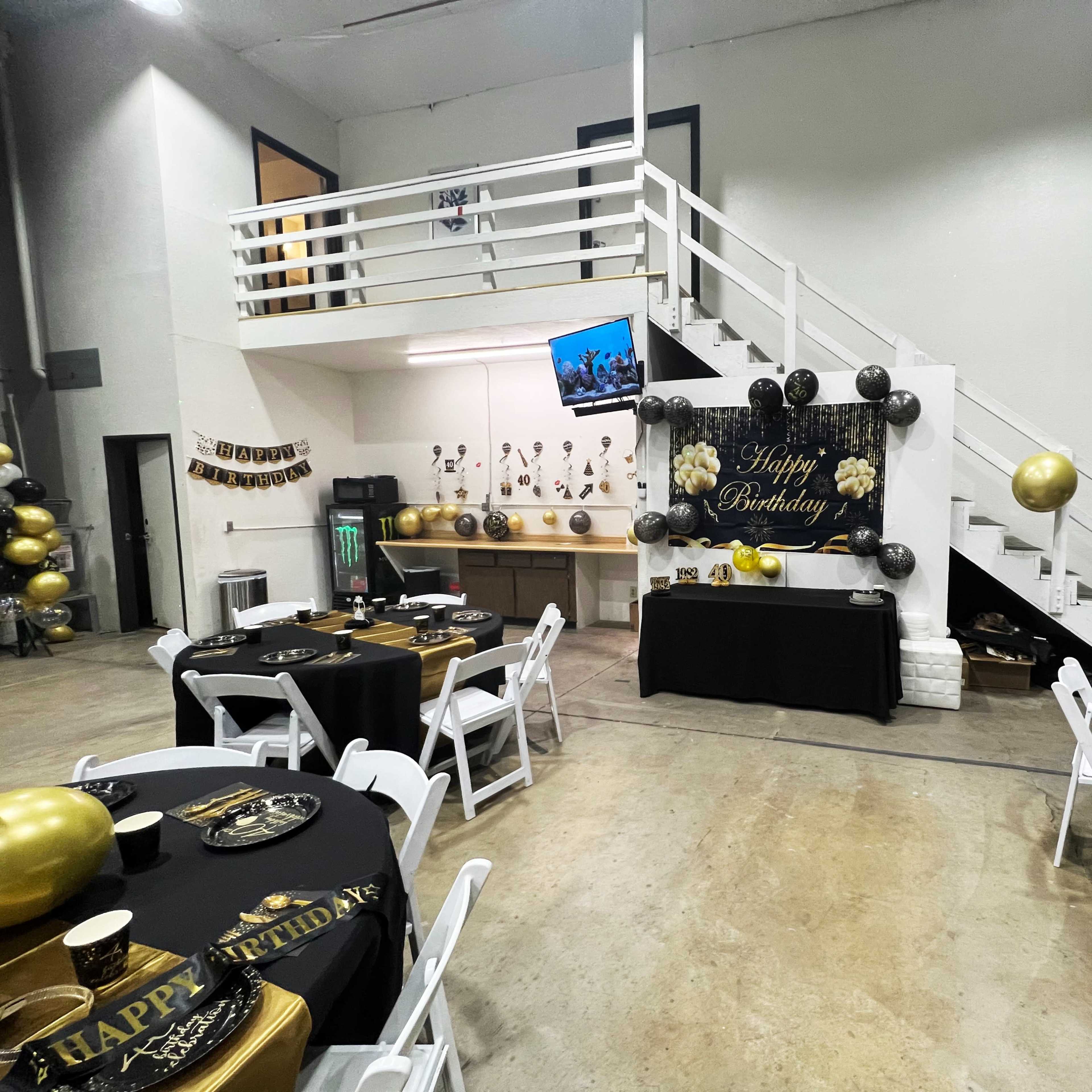 A birthday party setup is shown with black and gold decorations, tables set with tableware, and a large "Happy Birthday" banner displayed on the wall.