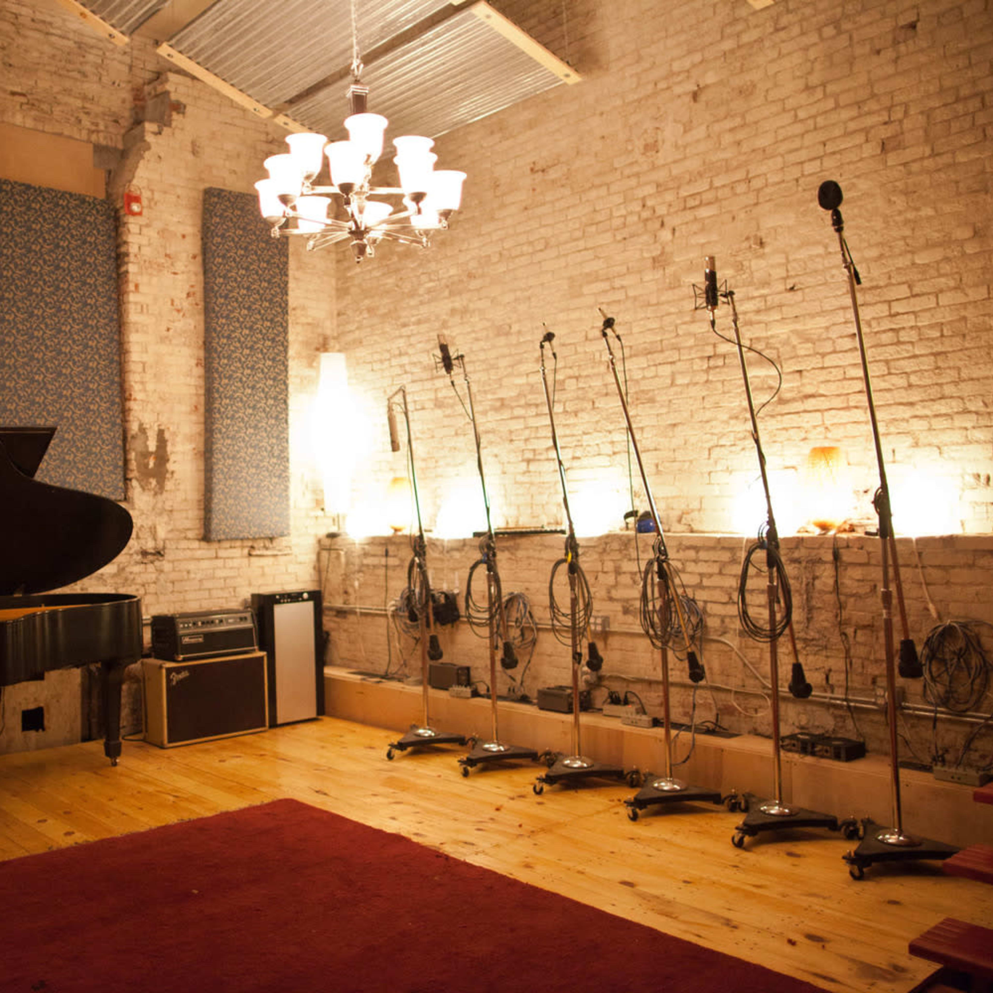 A music recording studio featuring a grand piano, several microphone stands, and a well-lit brick wall.