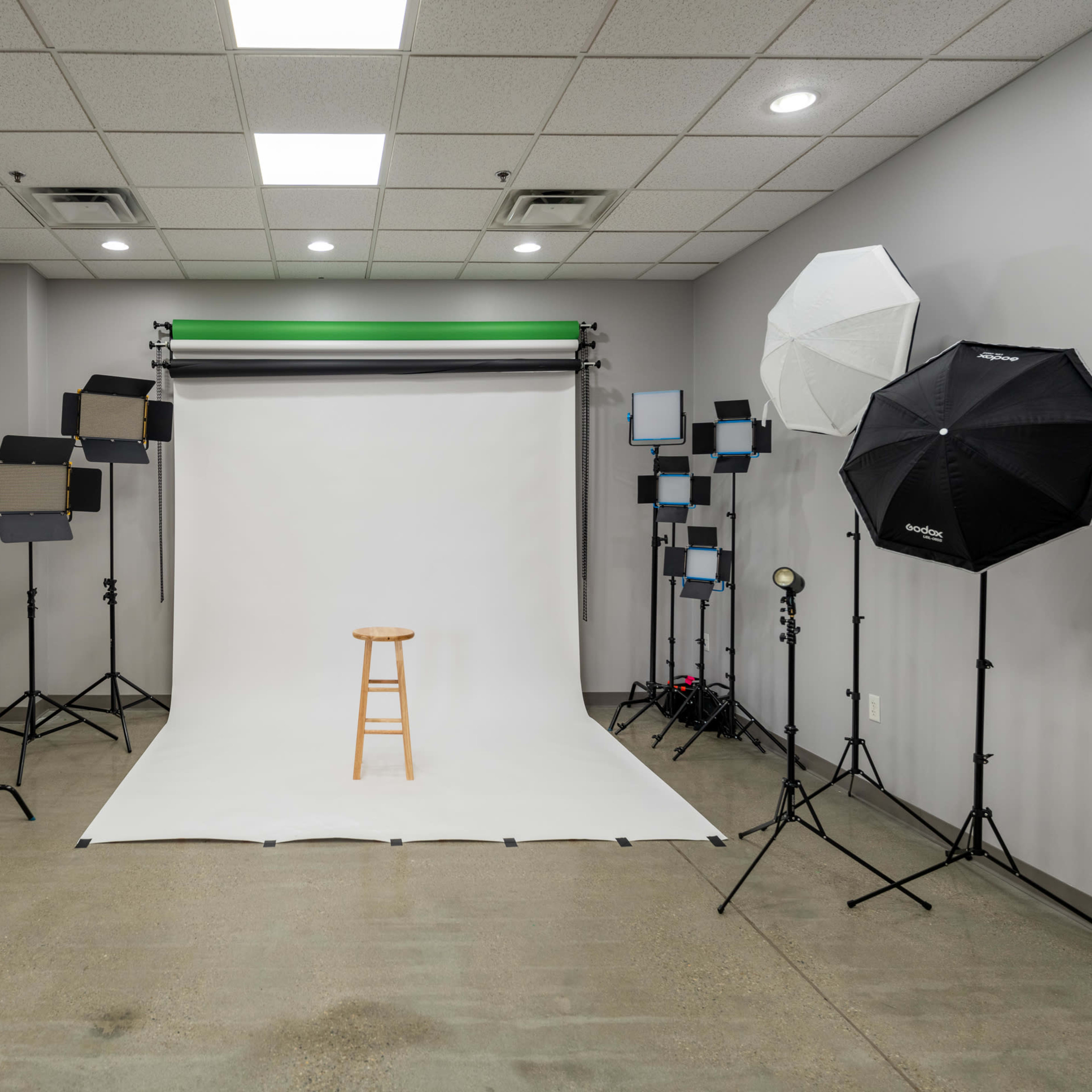 A photography studio is set up with a stool at the center, surrounded by various lighting equipment and backdrops.