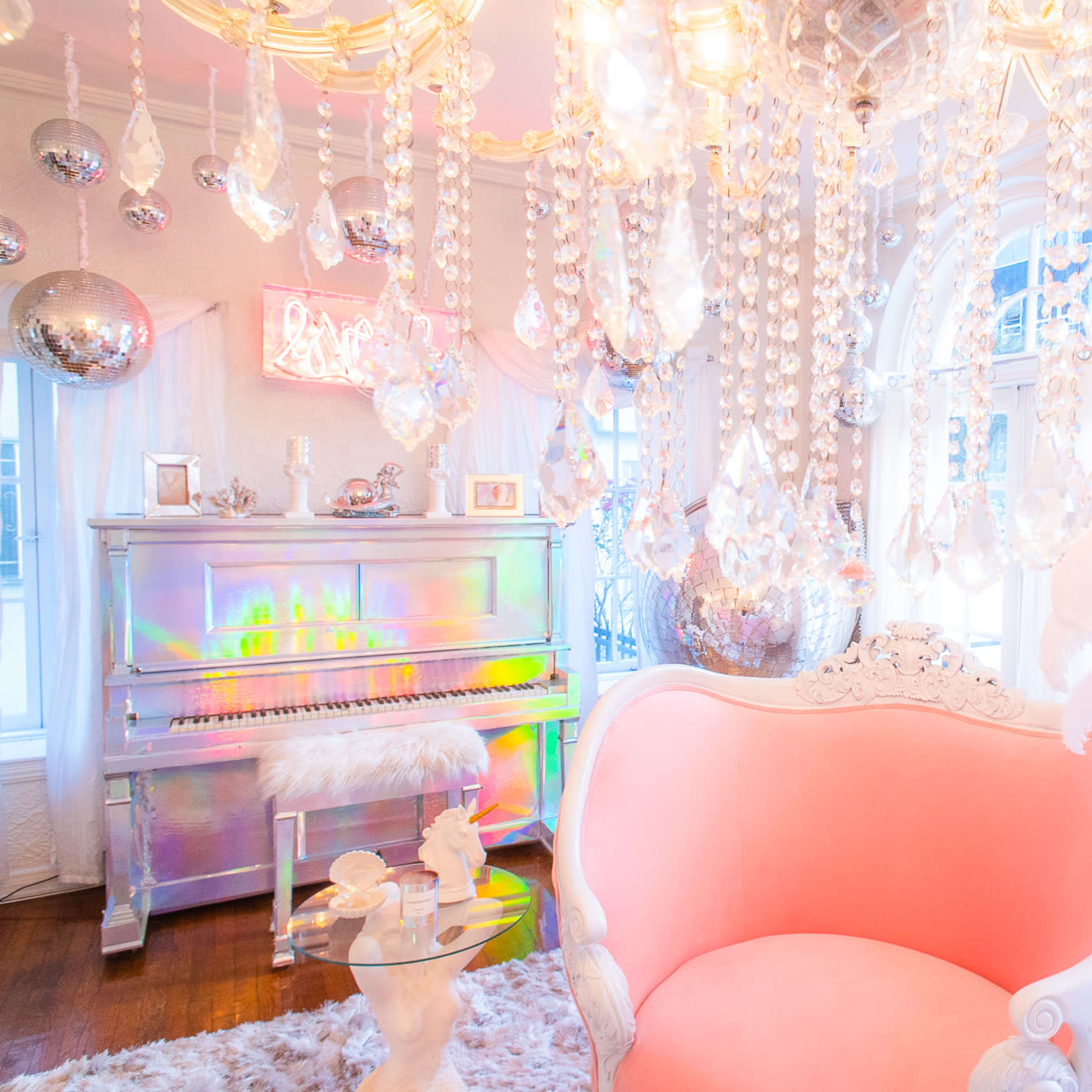 A brightly lit room featuring a pink upholstered sofa, a white piano adorned with colorful lights, and numerous hanging crystal decorations.