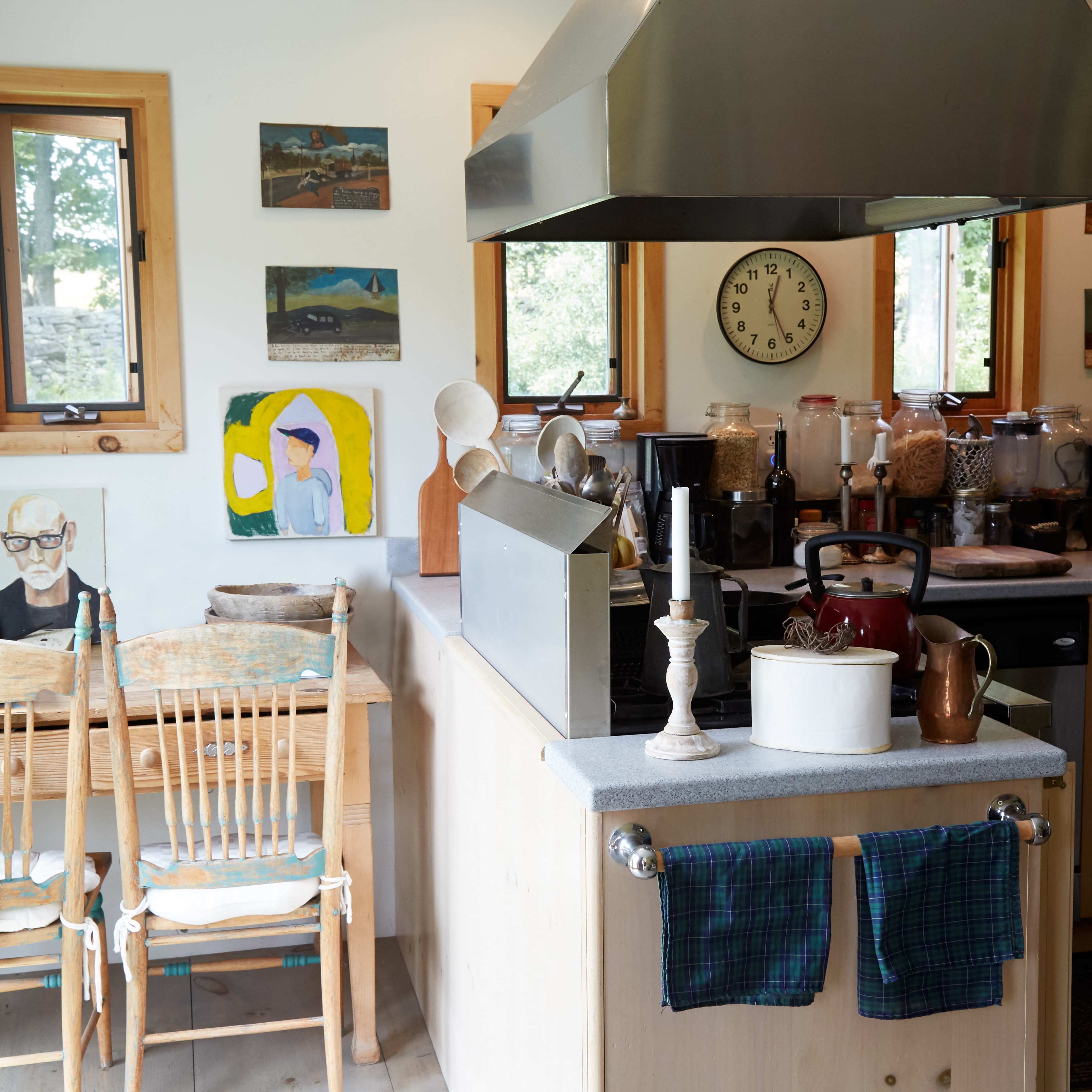 A kitchen with wooden cabinets, a central island with a stovetop, a table and chairs, and various artworks and kitchen items displayed on the walls and counters.
